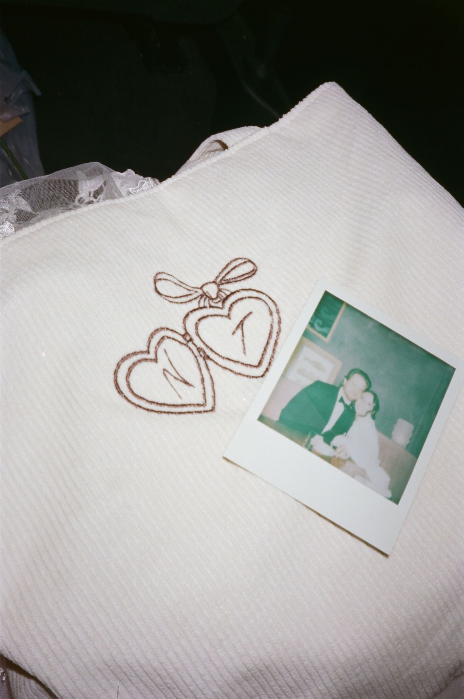 White knit sweater with embroidered heart locket design beside a Polaroid photo of a couple at a wedding.