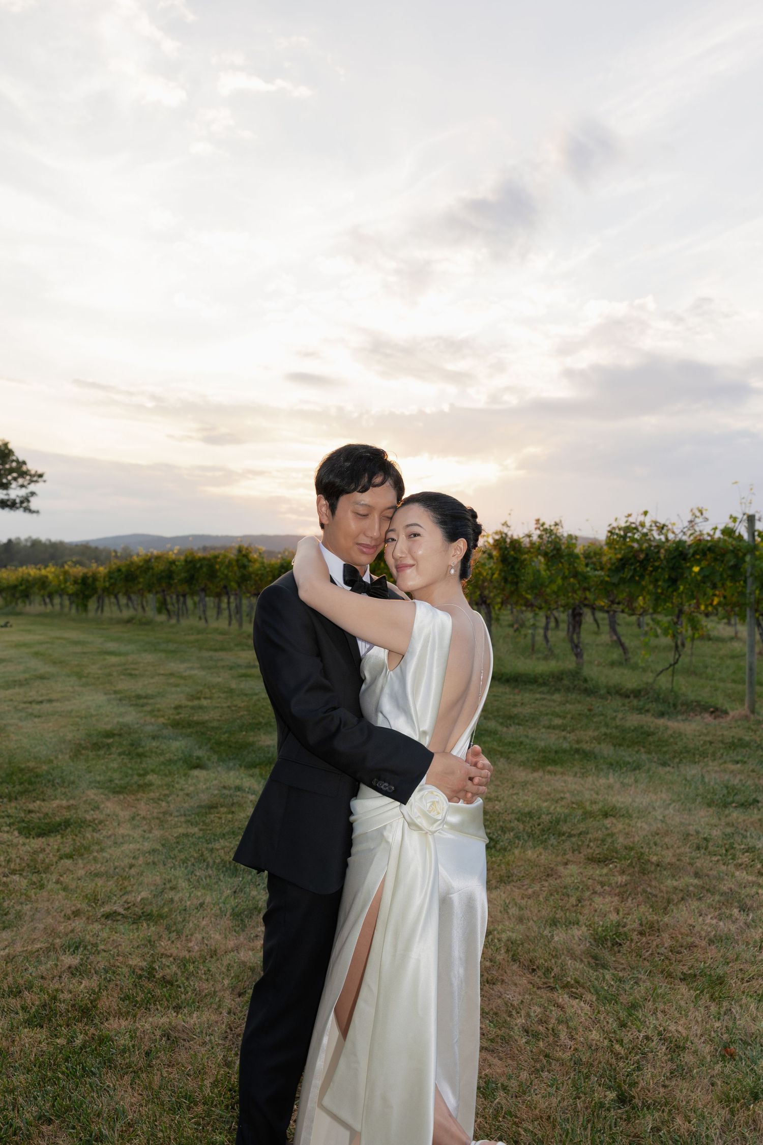Romantic couple embraces in a vineyard during sunset with mountains in the background.