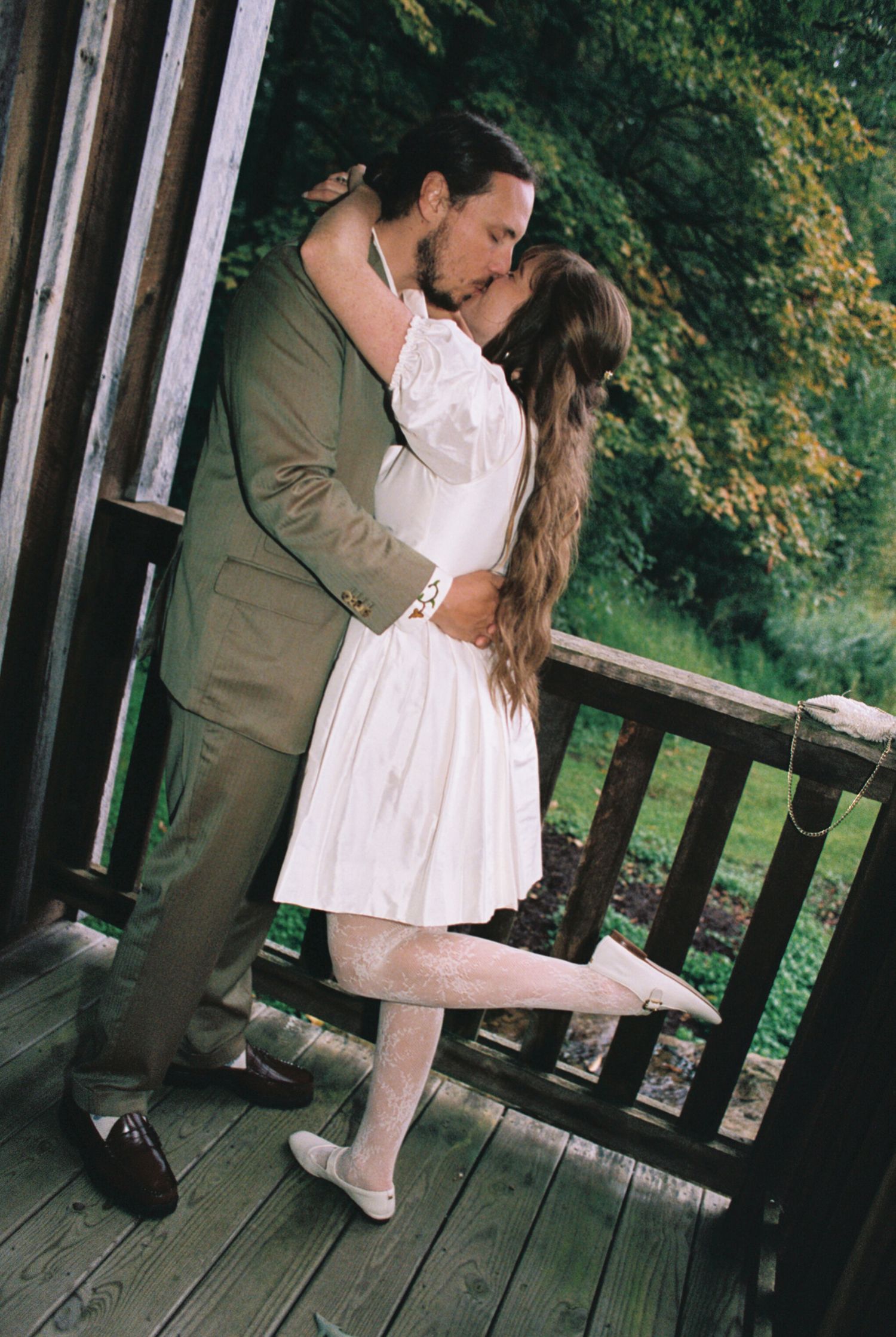 A romantic couple shares an intimate moment on a rustic wooden deck surrounded by greenery.