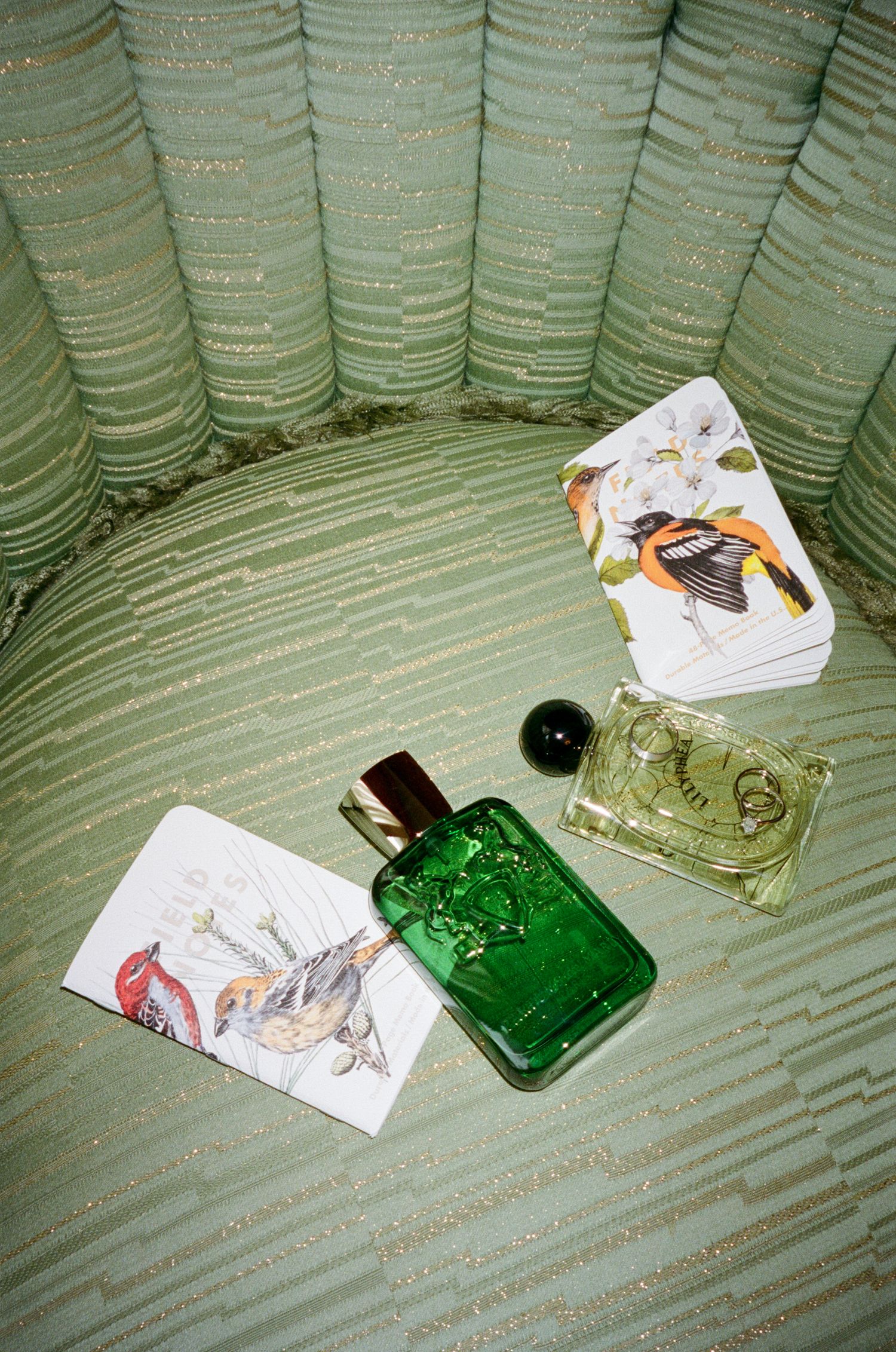 A green glass perfume bottle and crumpled paper trash sit on a mint green striped couch or chair cushion.