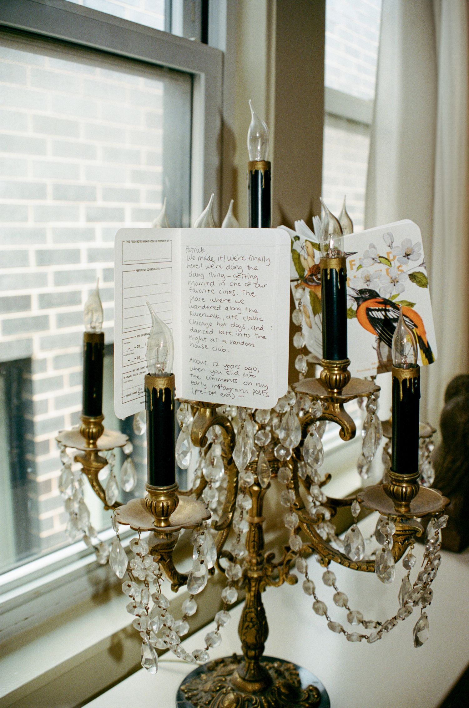 Ornate crystal chandelier with handwritten notes attached to it sits near a window with natural light streaming in.