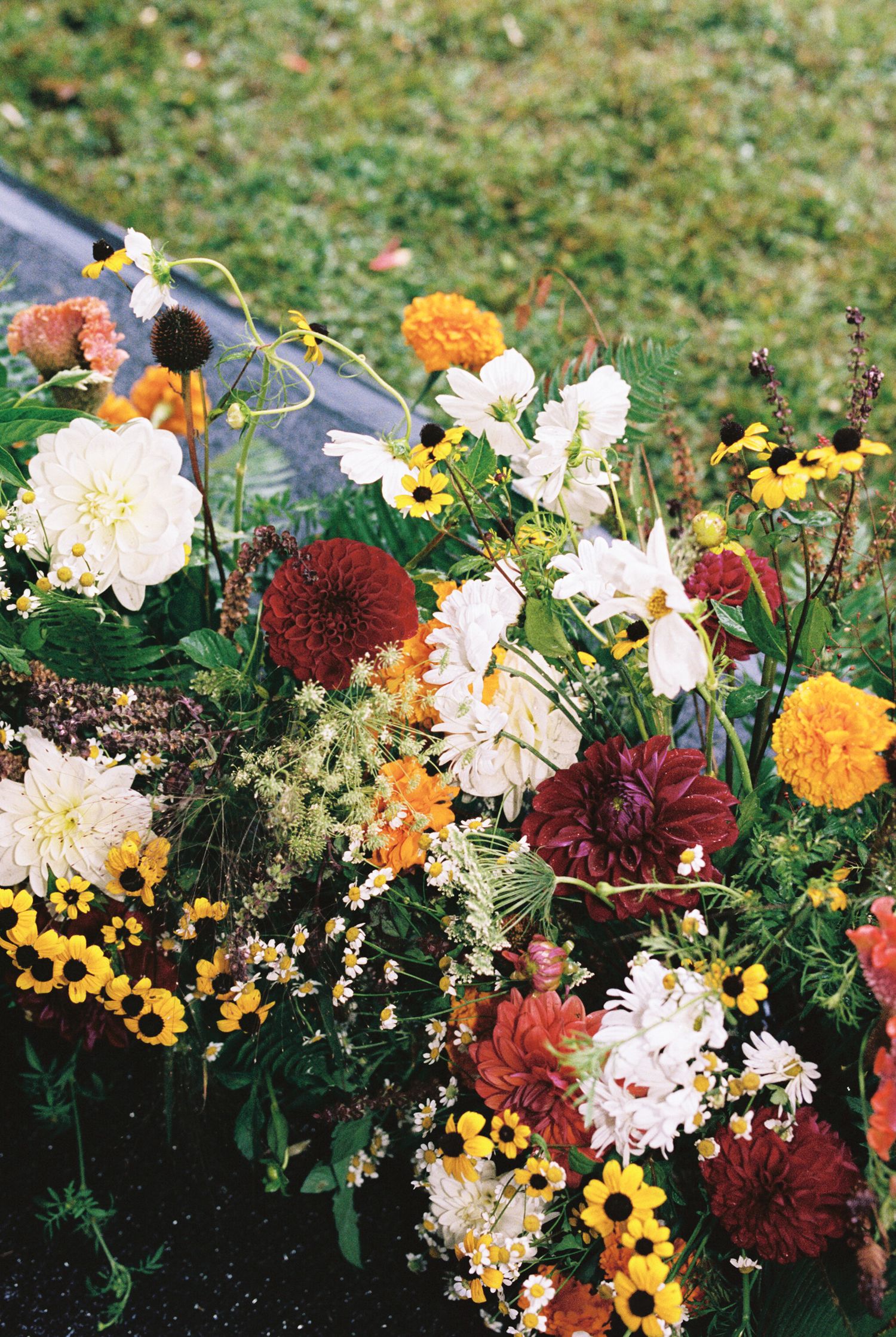 Colorful autumn floral arrangement featuring white daisies, burgundy dahlias, yellow sunflowers, and orange marigolds.