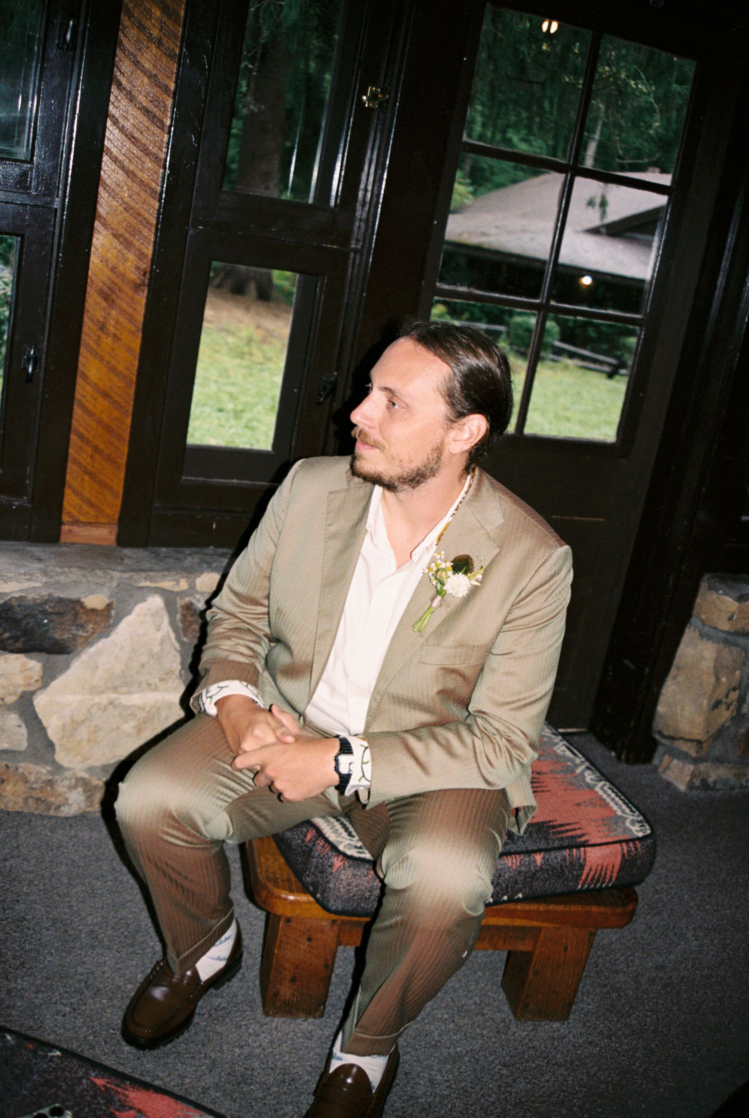 A person in a beige suit sits on a wooden bench in a sequence of four similar poses against a dark background.