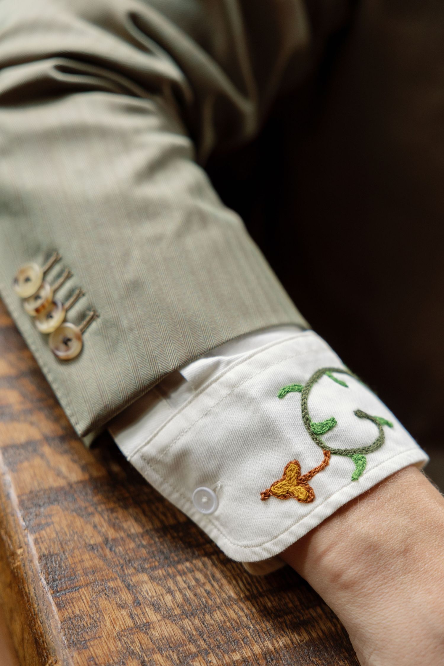A sequence of close-up shots showing embroidered details on a light gray shirt sleeve cuff resting on a wooden surface.
