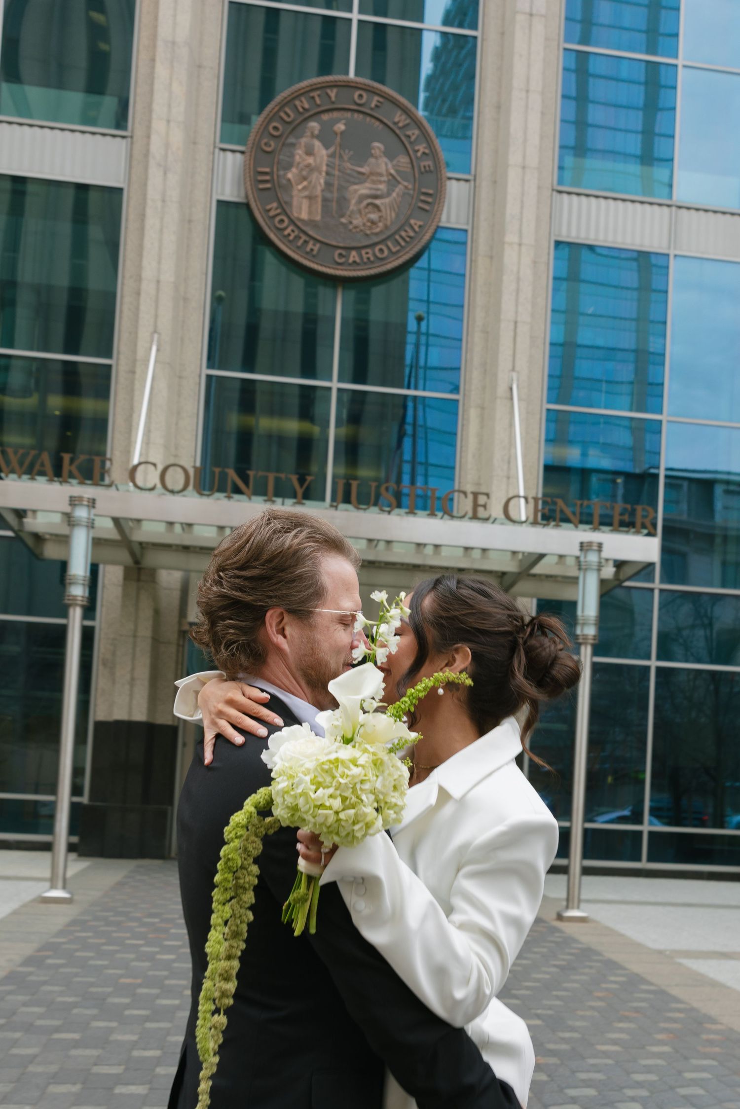 Couple sharing a romantic moment with bouquet outside Wake County Justice Center in North Carolina.