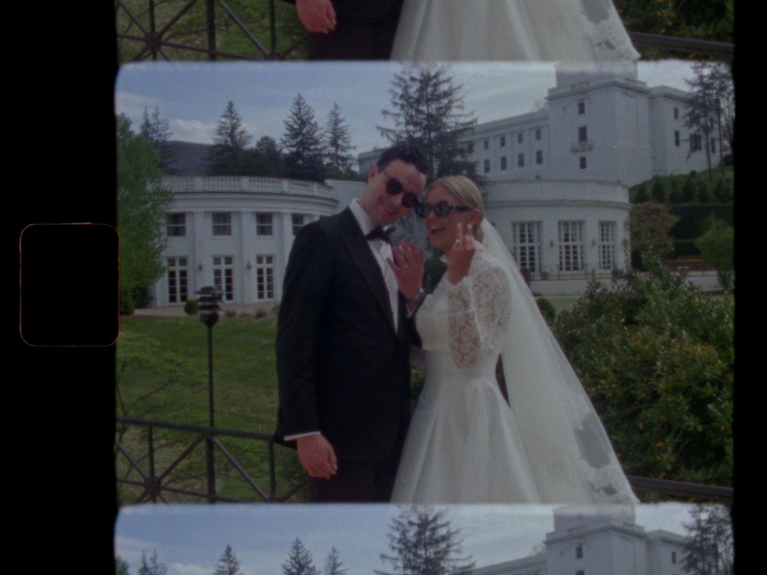 A bride and groom pose elegantly outside a grand white estate on their wedding day.