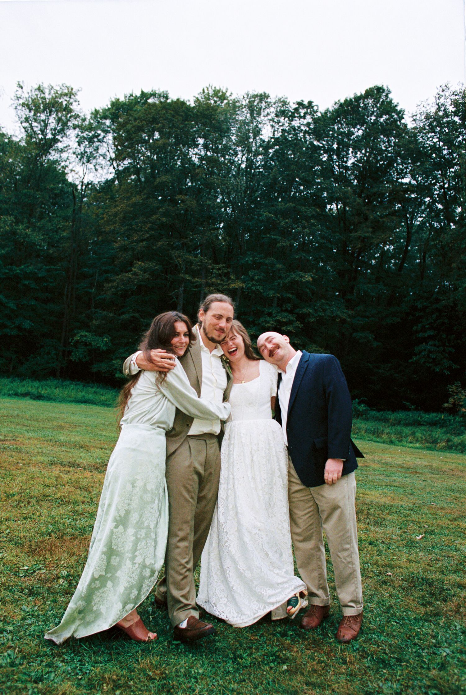 Group of people sitting together in a casual outdoor setting on grassy field with trees in background.