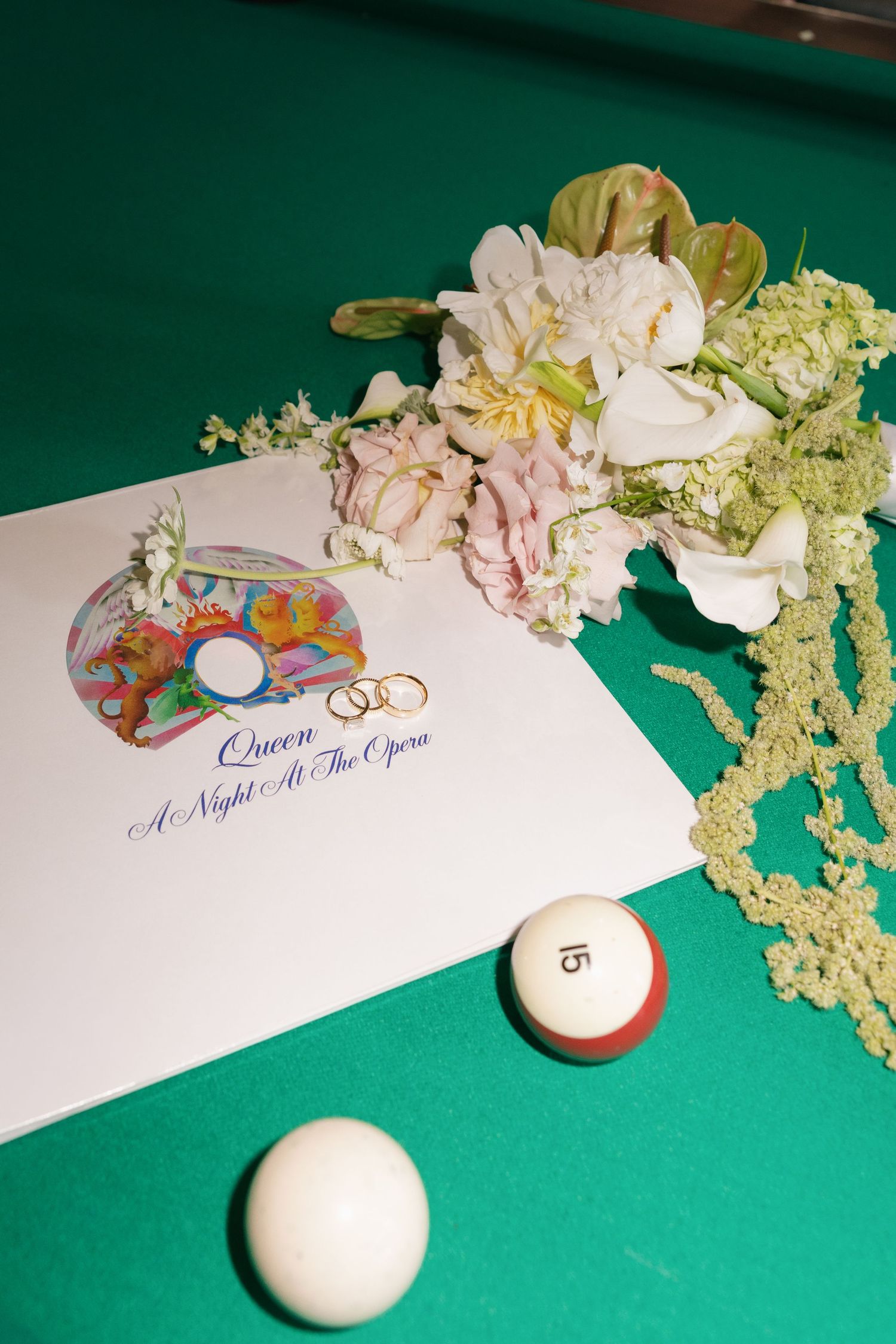 Queen A Night at the Opera album cover with wedding rings and a floral bouquet on a green pool table beside billiard balls.