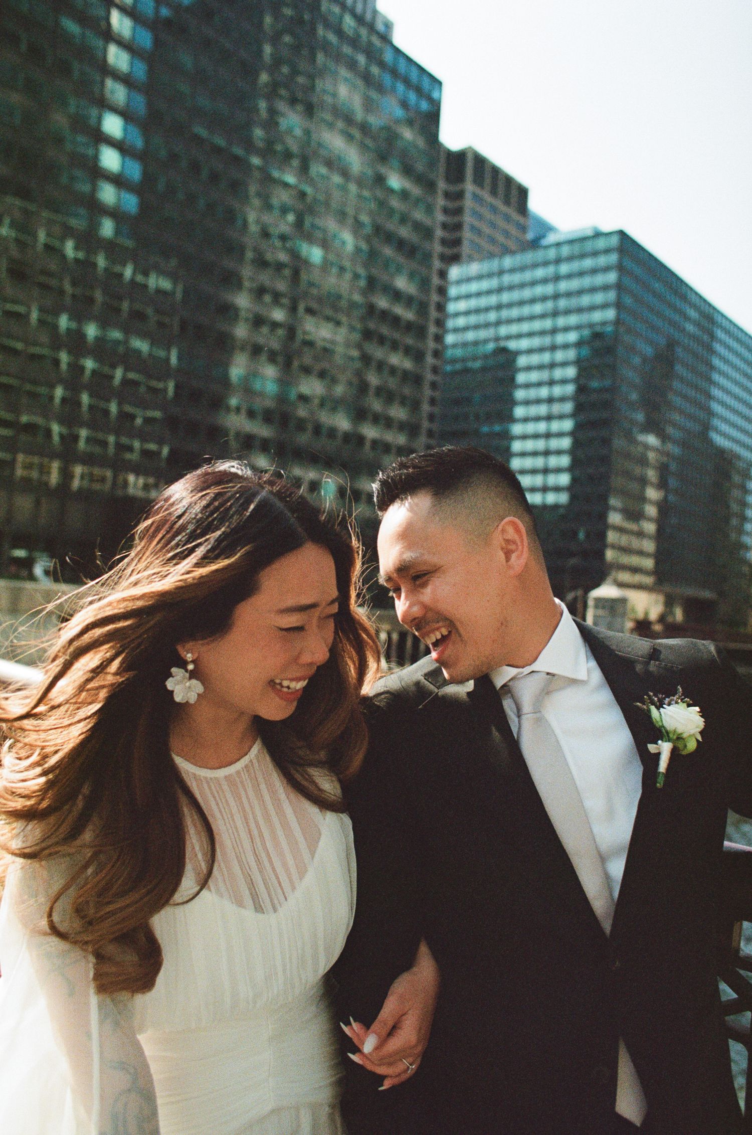A couple shares intimate moments in front of modern glass buildings during their wedding photoshoot.