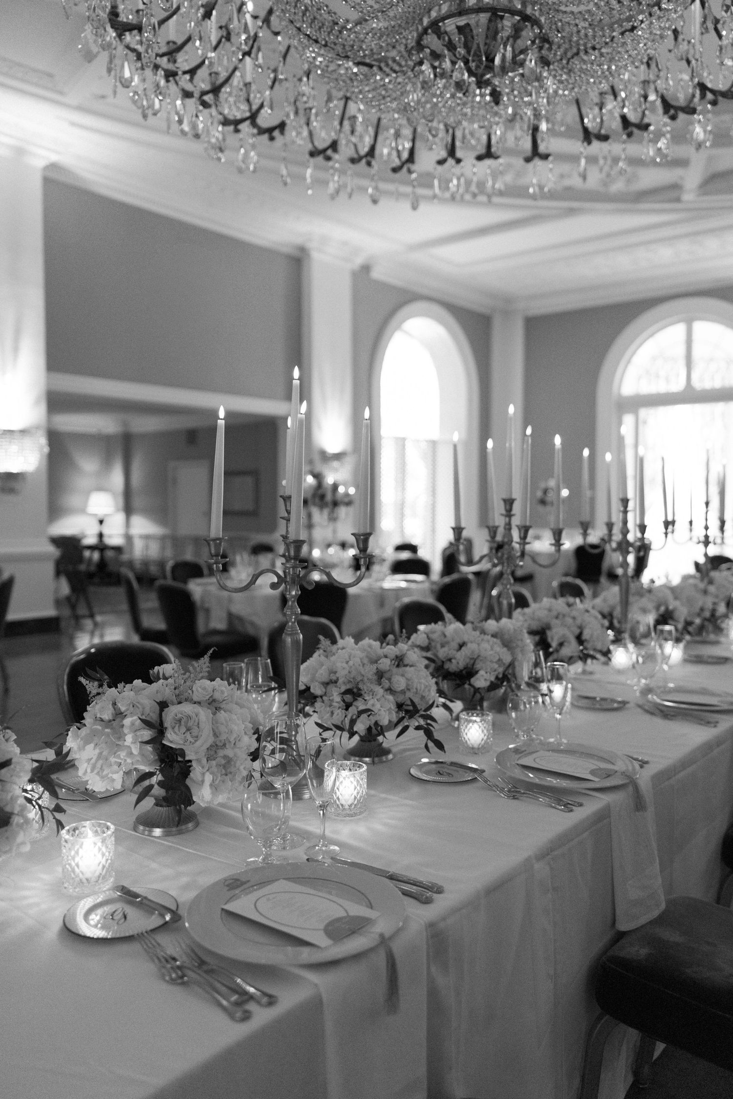 Elegant black and white wedding reception table with candelabras, floral centerpieces, and crystal chandelier in a grand ballroom.