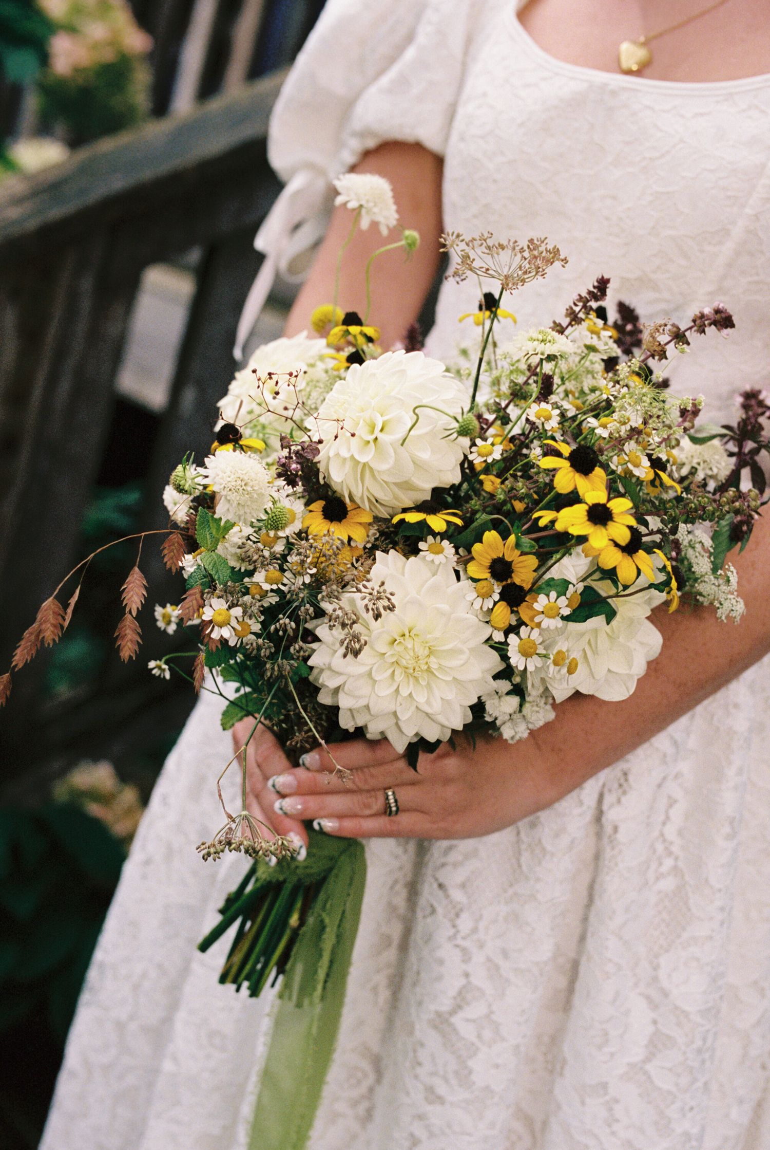 A white and yellow bridal bouquet featuring dahlias and wildflowers with green ribbon wrapped stems.