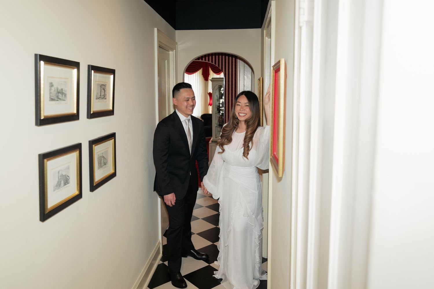 Two people stand in a hallway with framed artwork on the walls during what appears to be a gallery viewing.