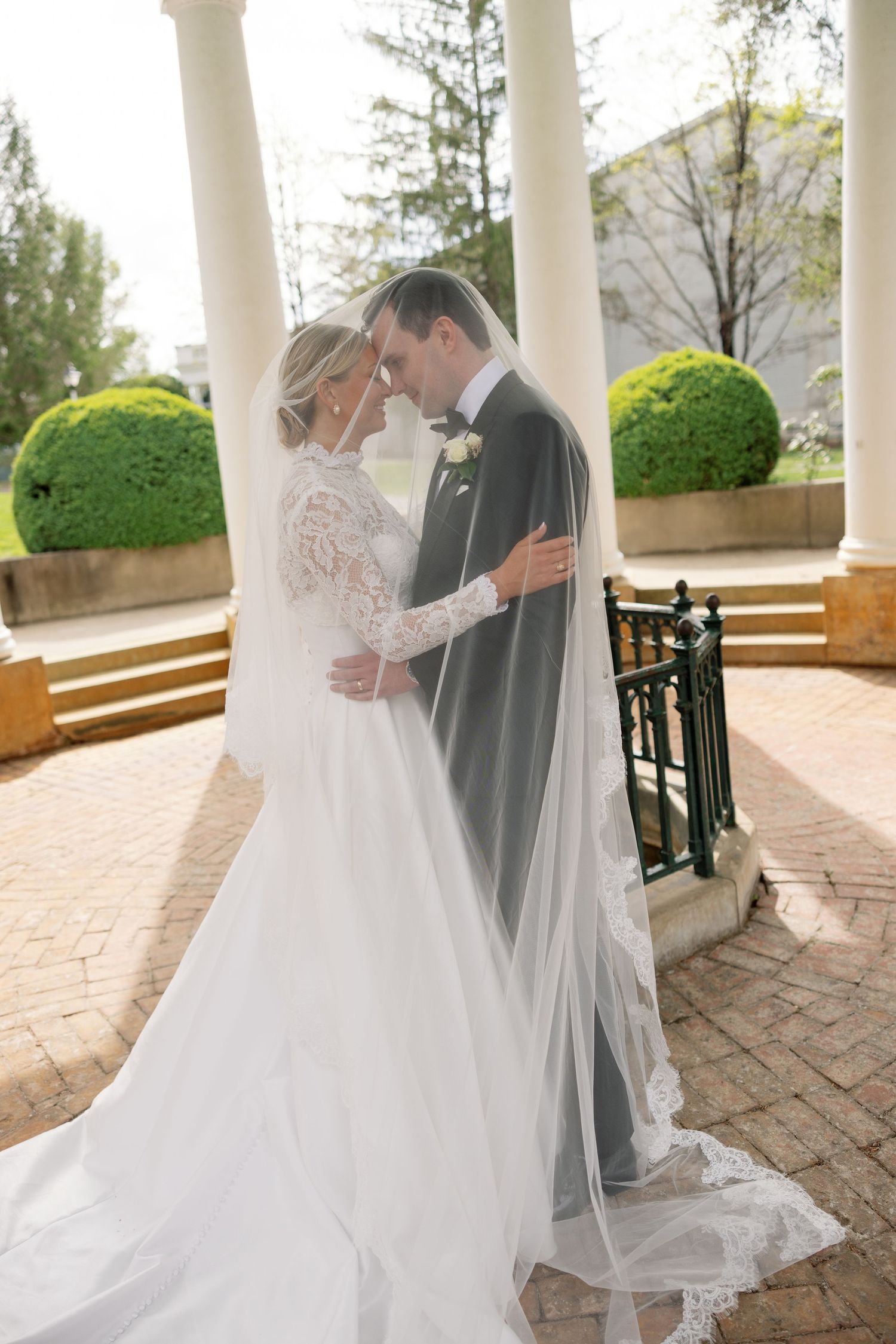 Bride and groom share a romantic moment under a white gazebo, her lace gown and veil flowing elegantly.