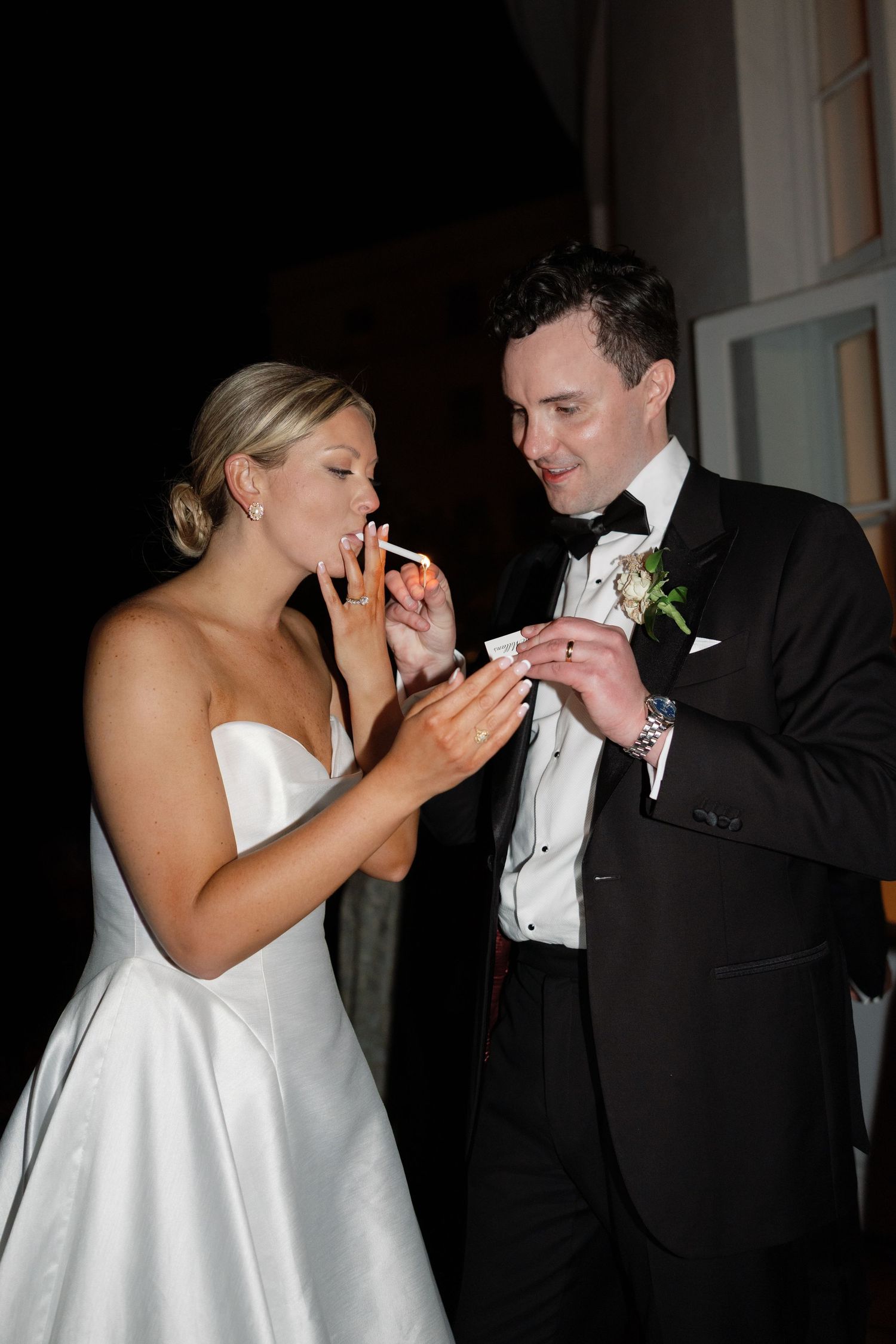 Bride and groom sharing wedding cake at their elegant black-tie reception, smiling joyfully.