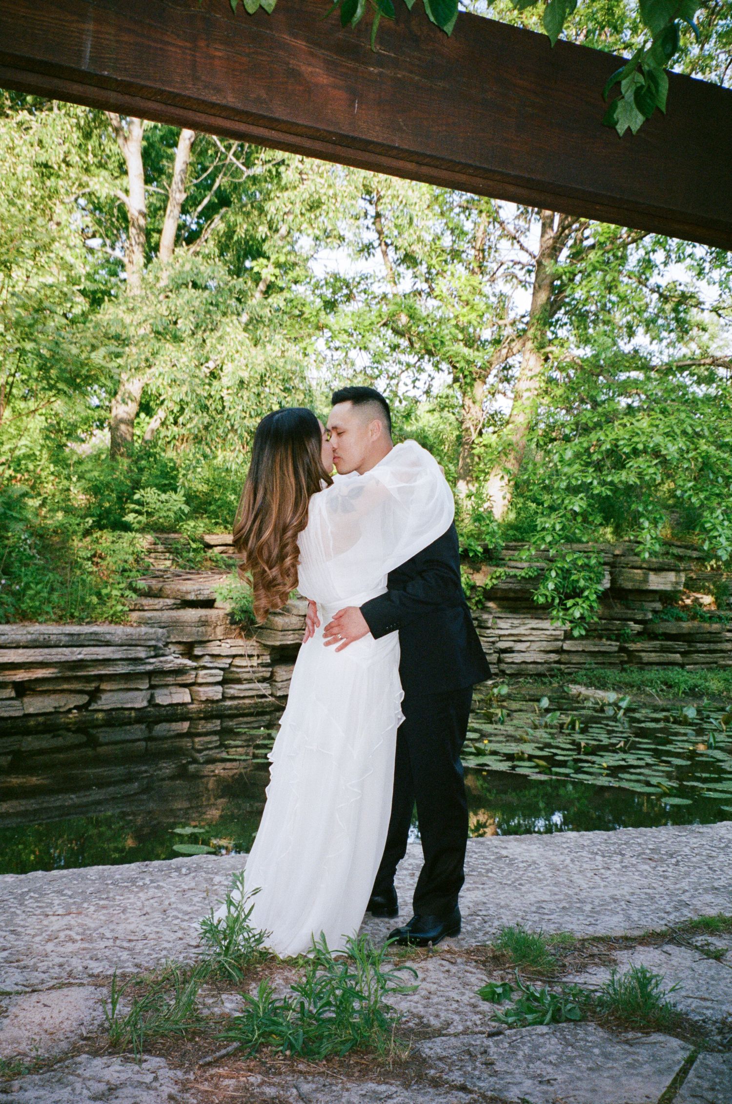 A romantic couple shares an intimate dance moment in a rustic outdoor setting with stone walls and greenery.