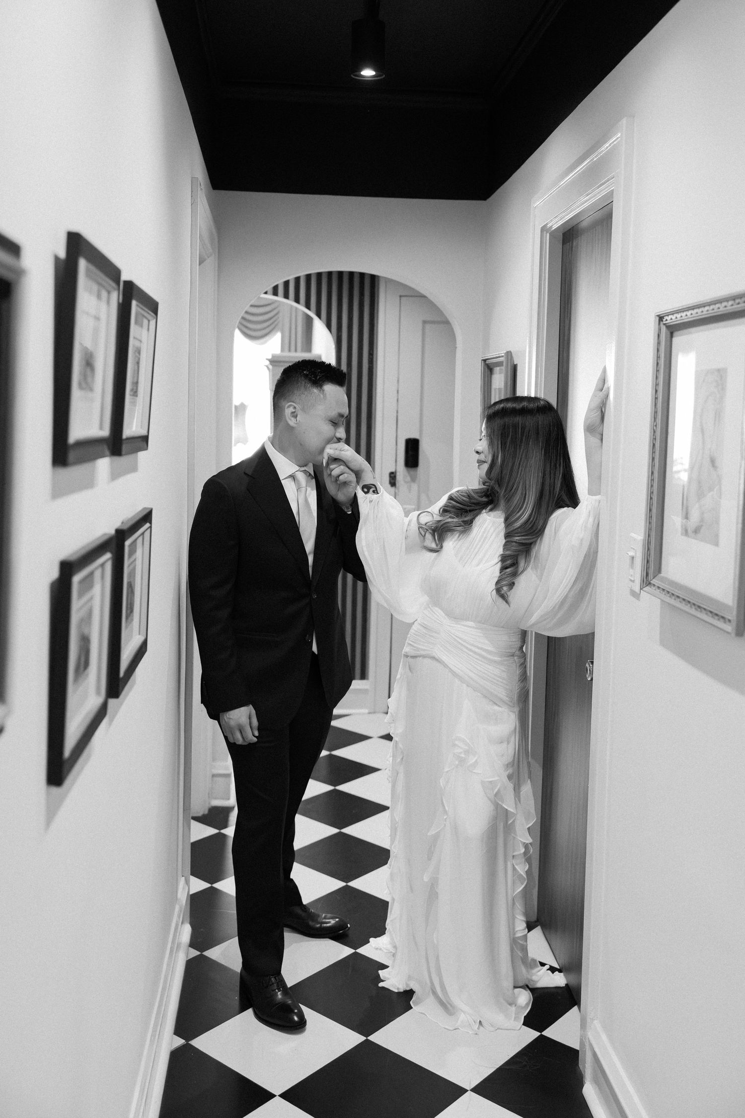 A black and white photo series shows a couple in wedding attire walking down a hallway with checkered floors and artwork.