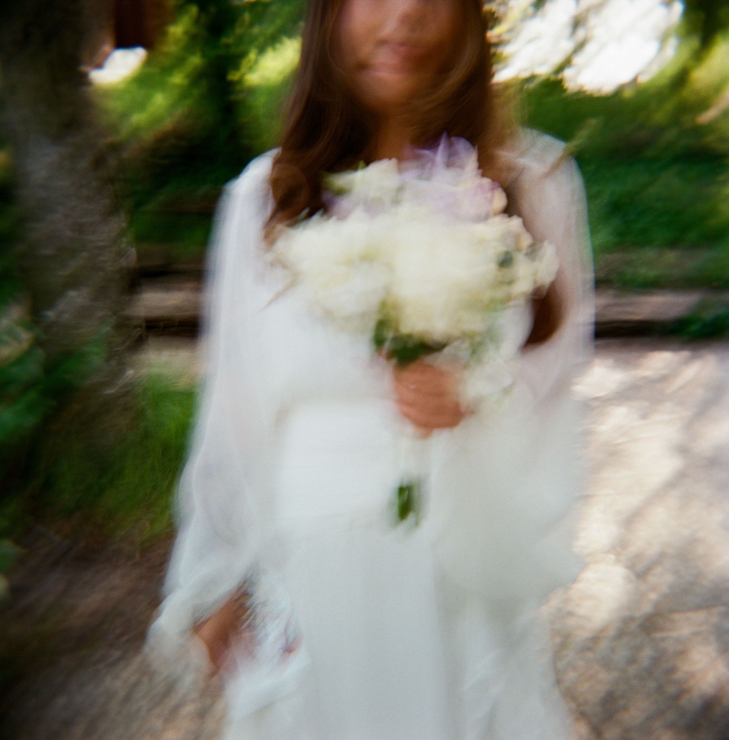 Bride in flowing white wedding dress twirls outdoors in a garden setting with natural sunlight filtering through trees.