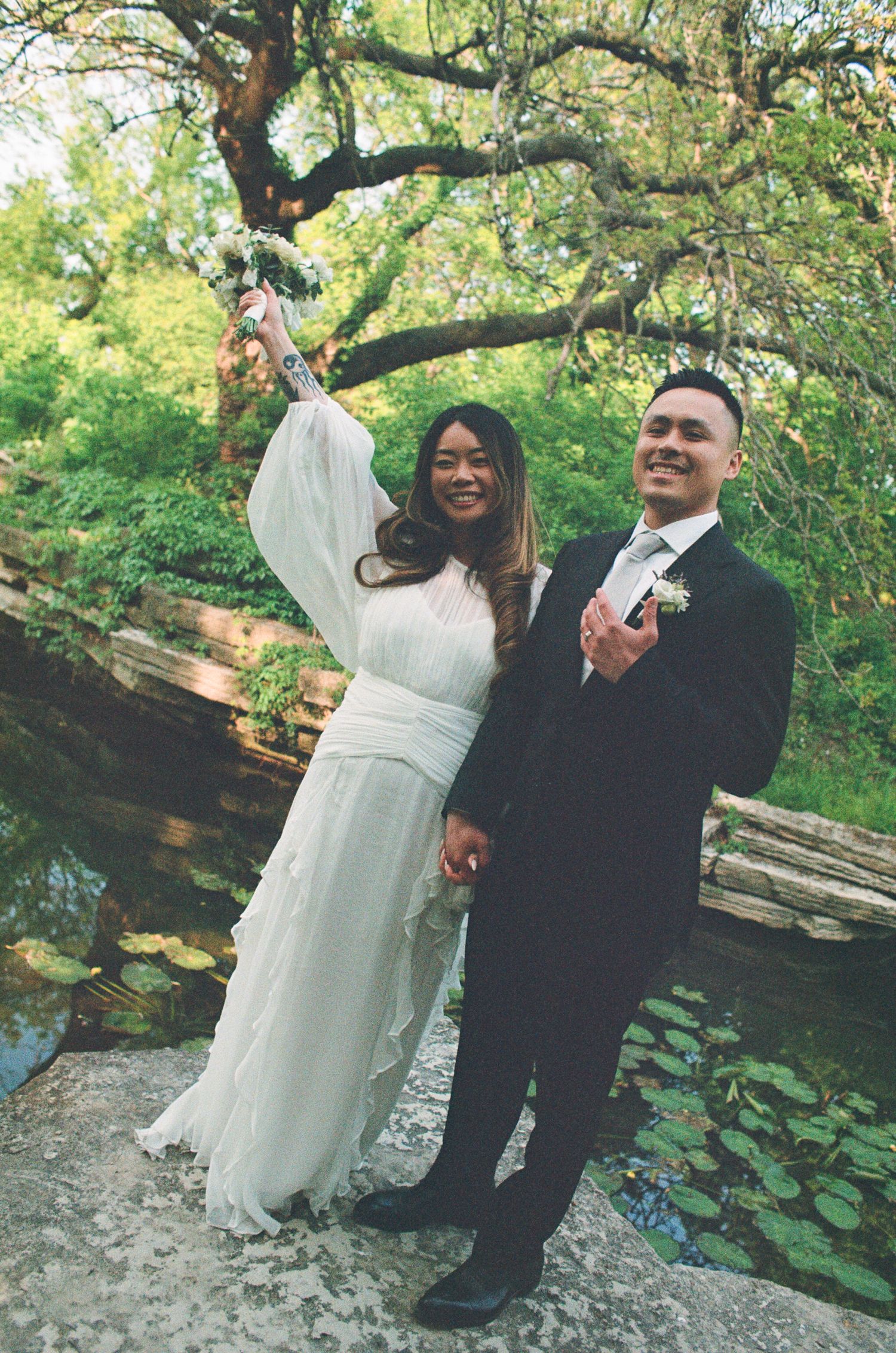 A couple shares a romantic moment together on a stone path surrounded by lush green foliage in a garden setting.