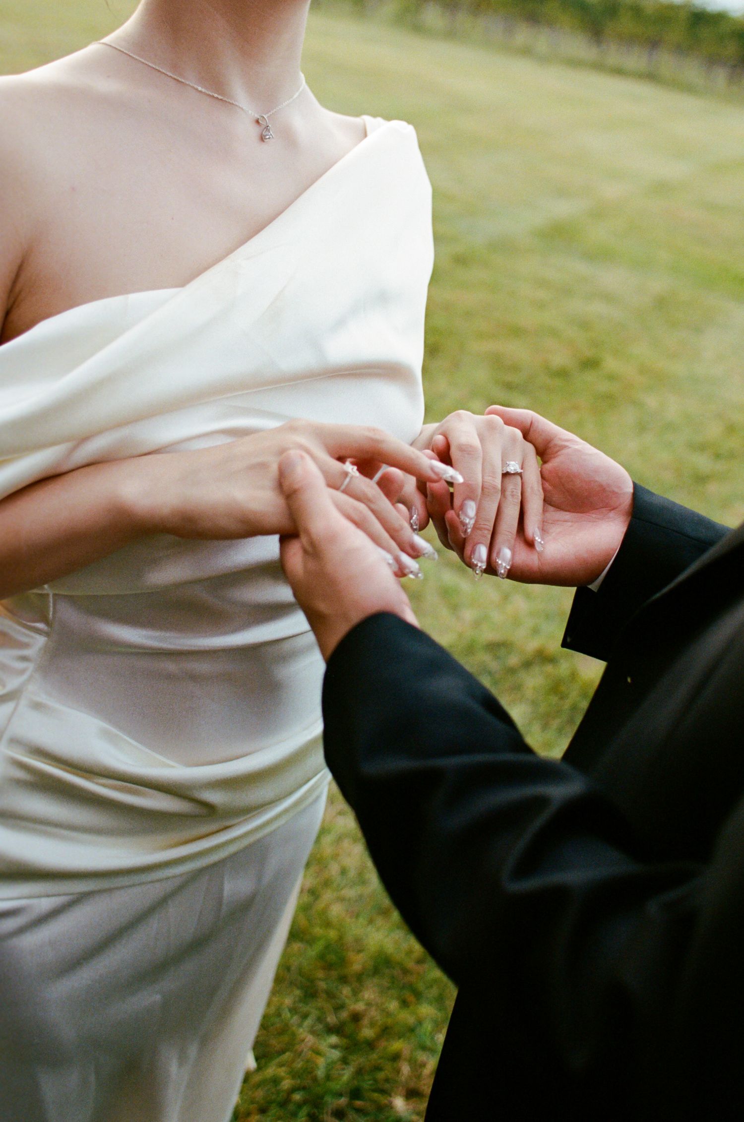 Close-up sequence of hands exchanging wedding rings during an outdoor ceremony on grass.