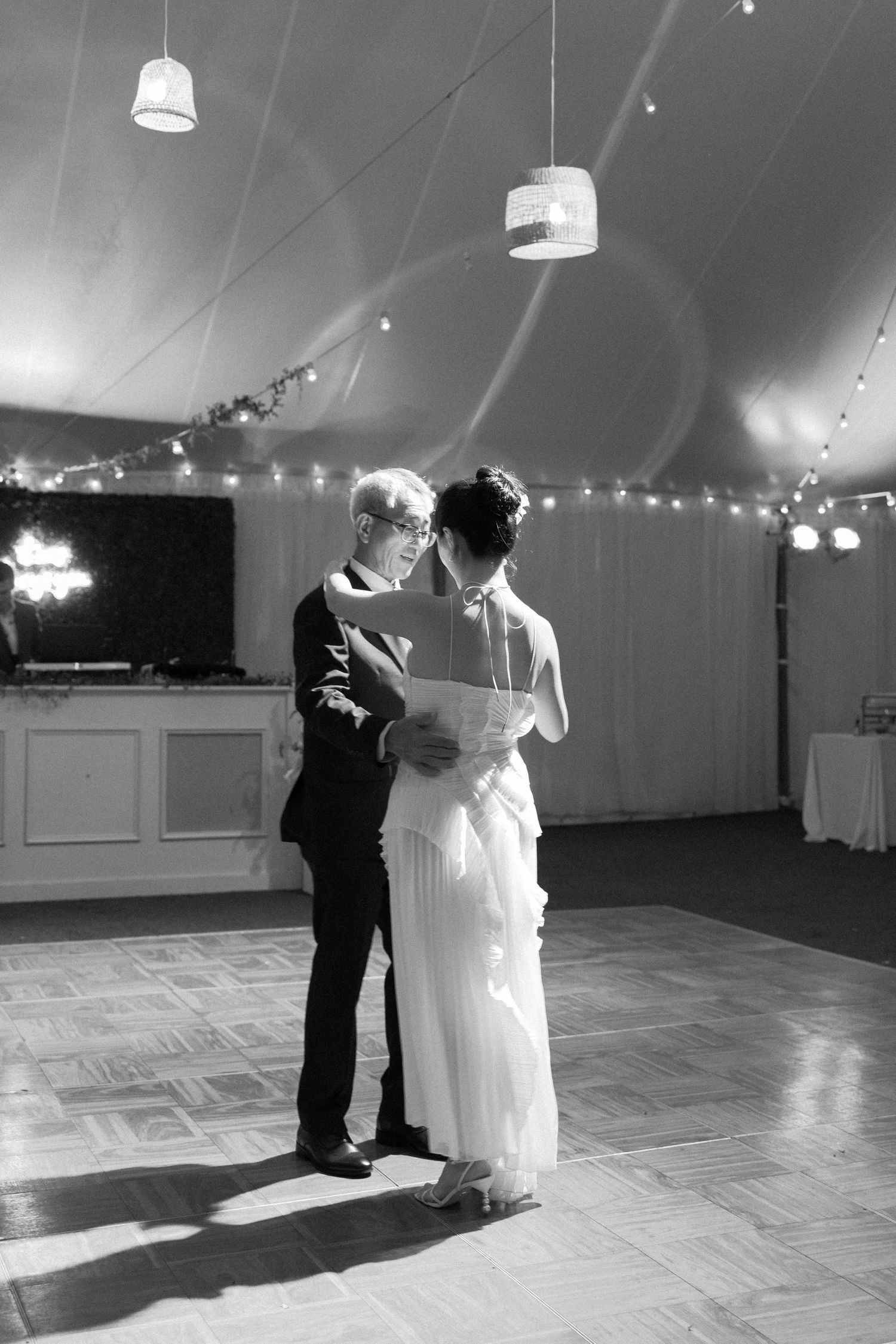 A couple shares their first dance together in a white tent reception venue with string lights overhead.