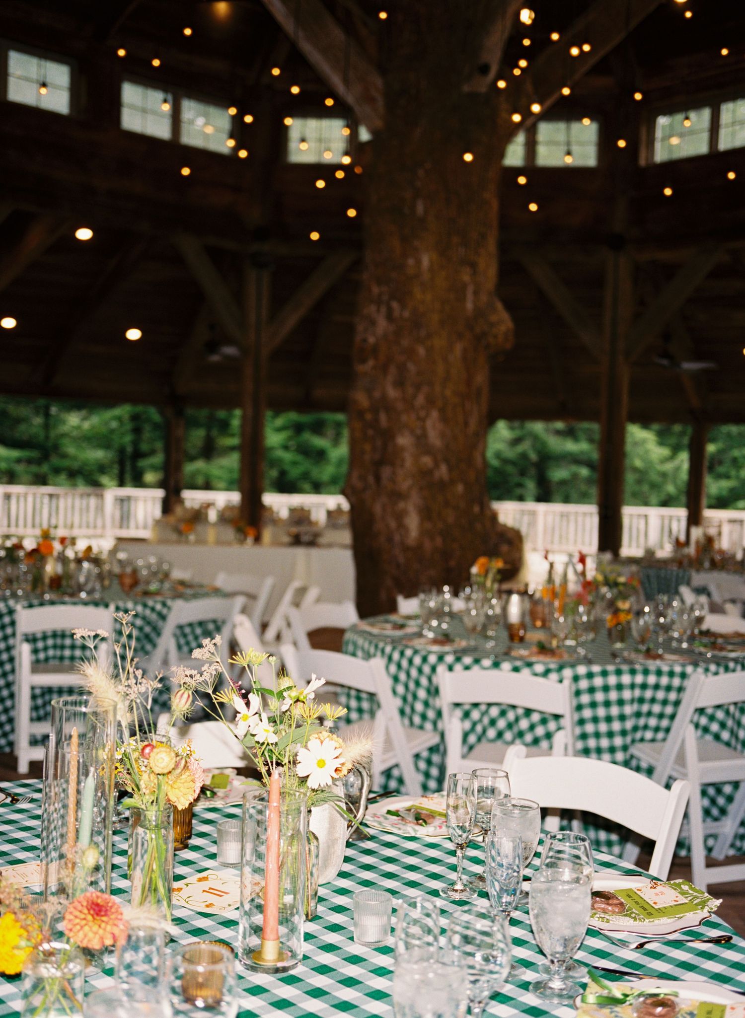 Wedding reception tables set with green checkered tablecloths and white chairs in a rustic indoor venue.