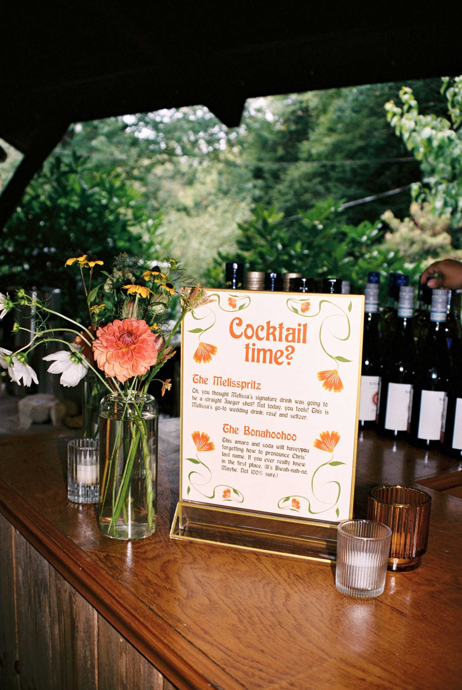 Wooden bar counter decorated with orange floral signs and mason jar centerpieces for a cocktail service setup.