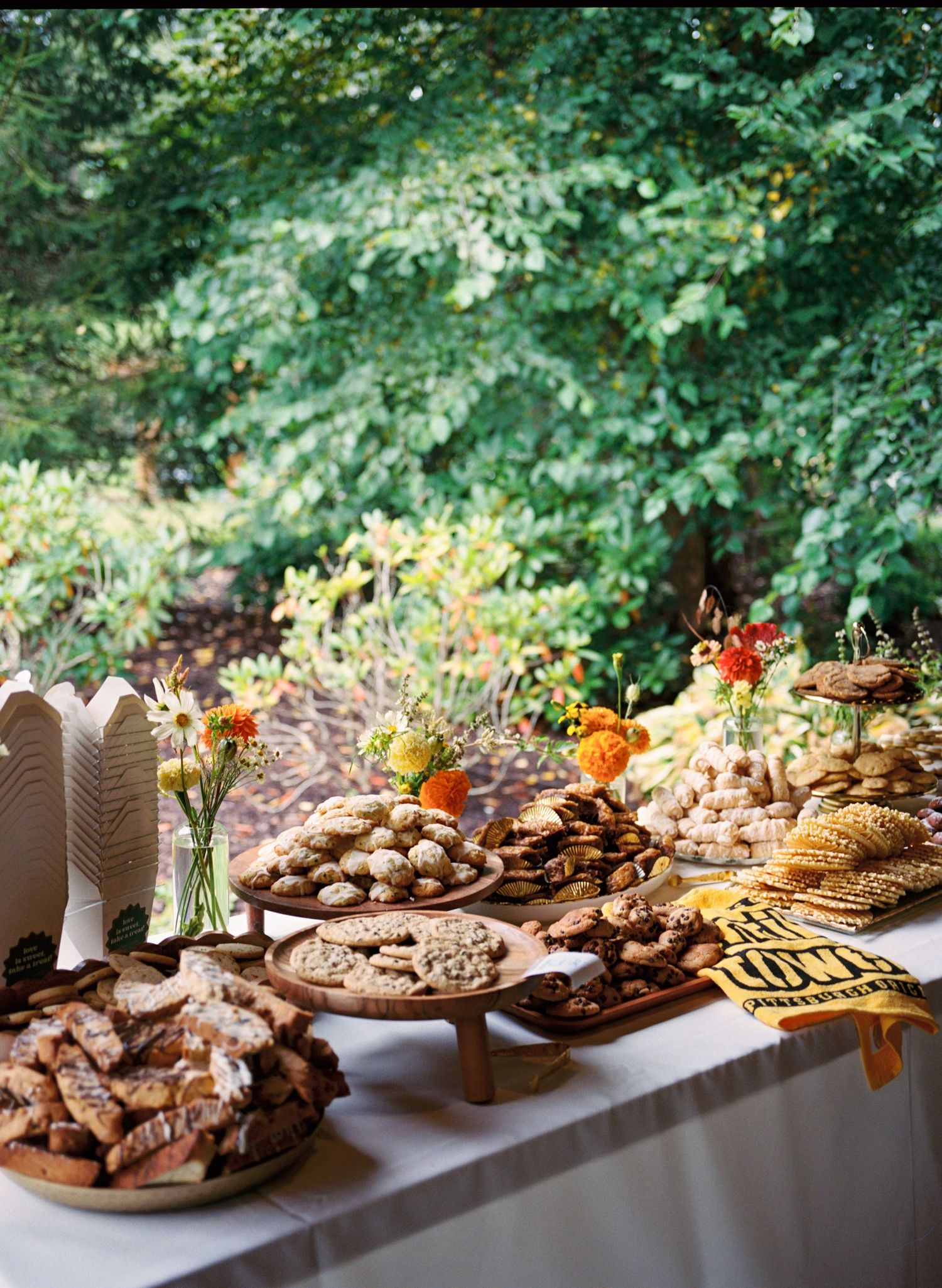 A rustic dessert table display features an assortment of cookies, pastries, and floral arrangements in warm autumn colors.