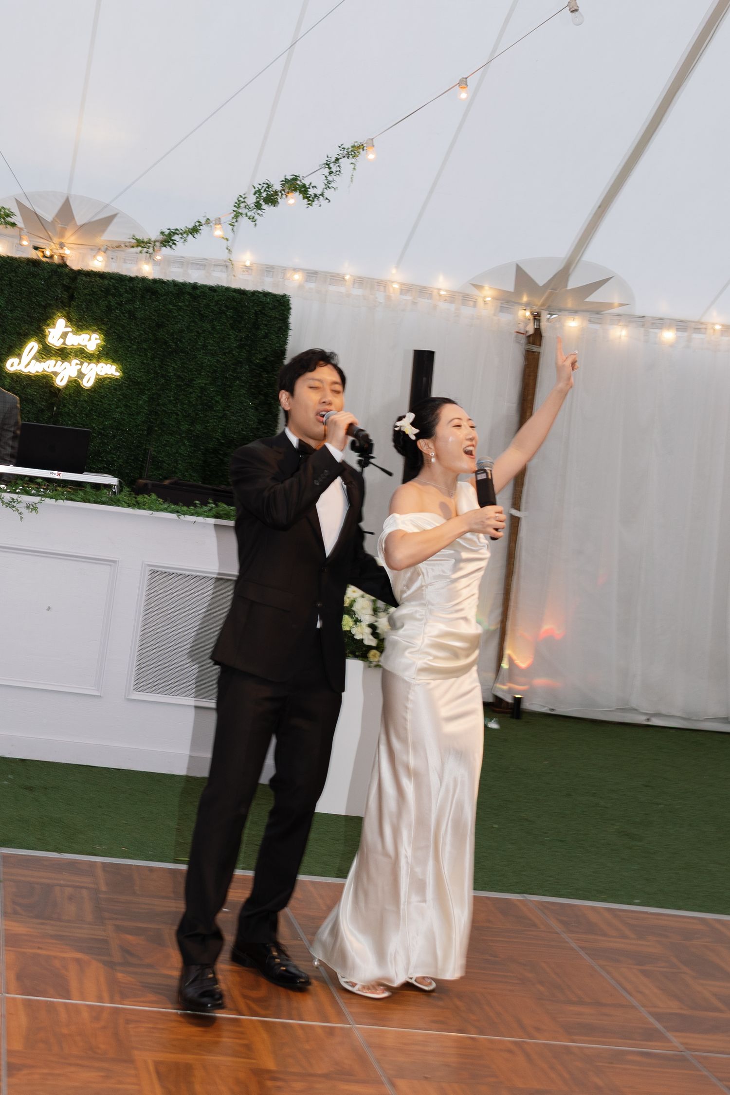 Wedding couple dances joyfully together on a decorated dance floor under twinkling lights at an indoor reception.