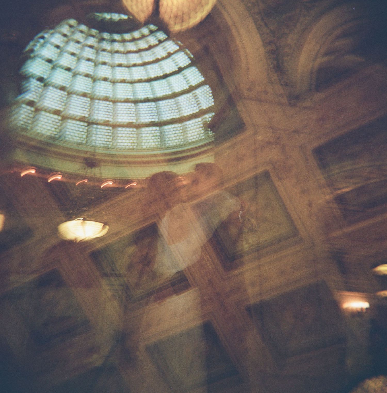 Ornate glass dome ceiling with dramatic lighting and architectural details in a historic building interior.