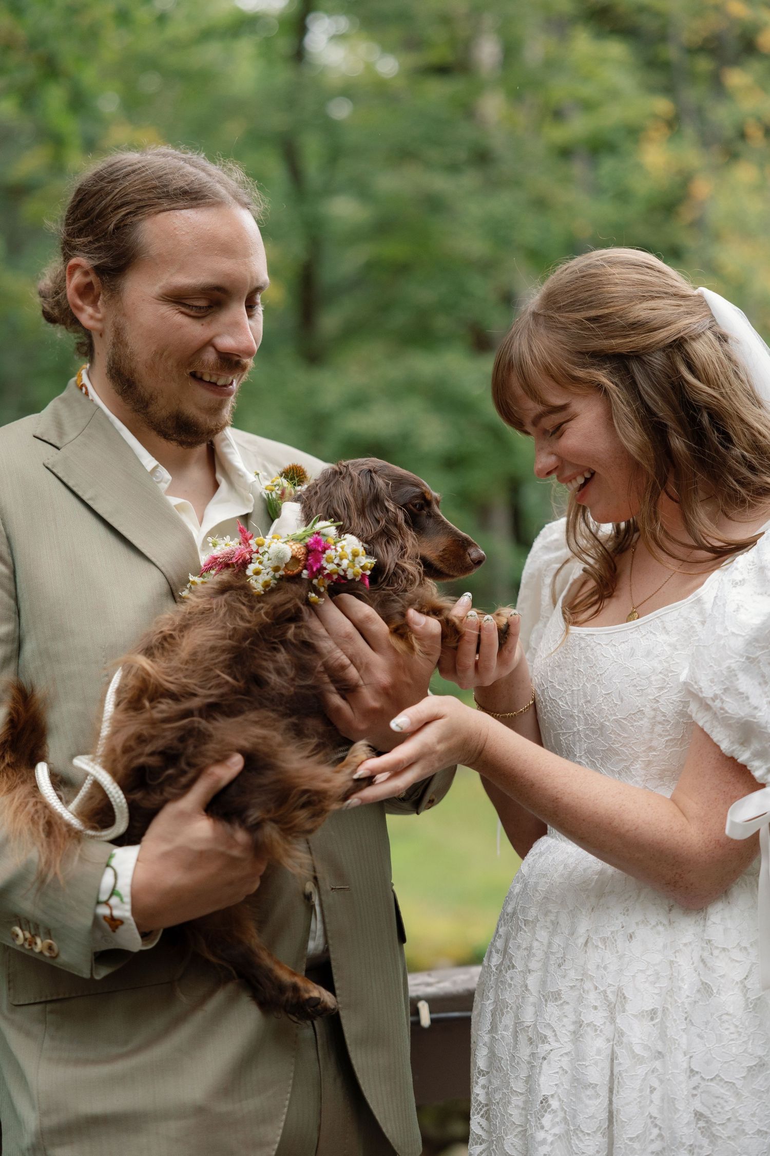 A couple in wedding attire shares a joyful moment with their brown dog during an outdoor photo session.