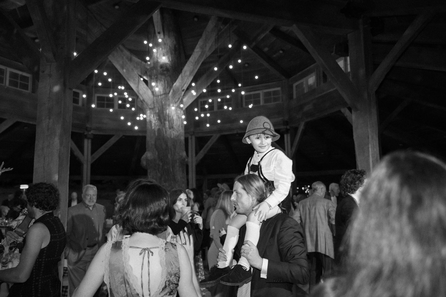 Black and white photo of a dance celebration at a rustic barn venue with string lights overhead.