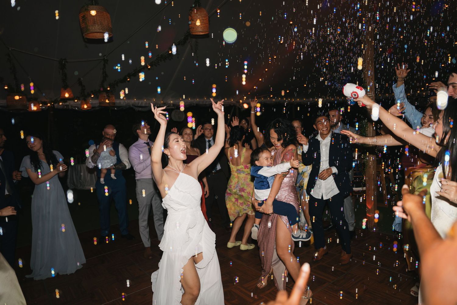 Wedding guests dancing and celebrating on a dark dance floor illuminated by glowing lights and disco effects.