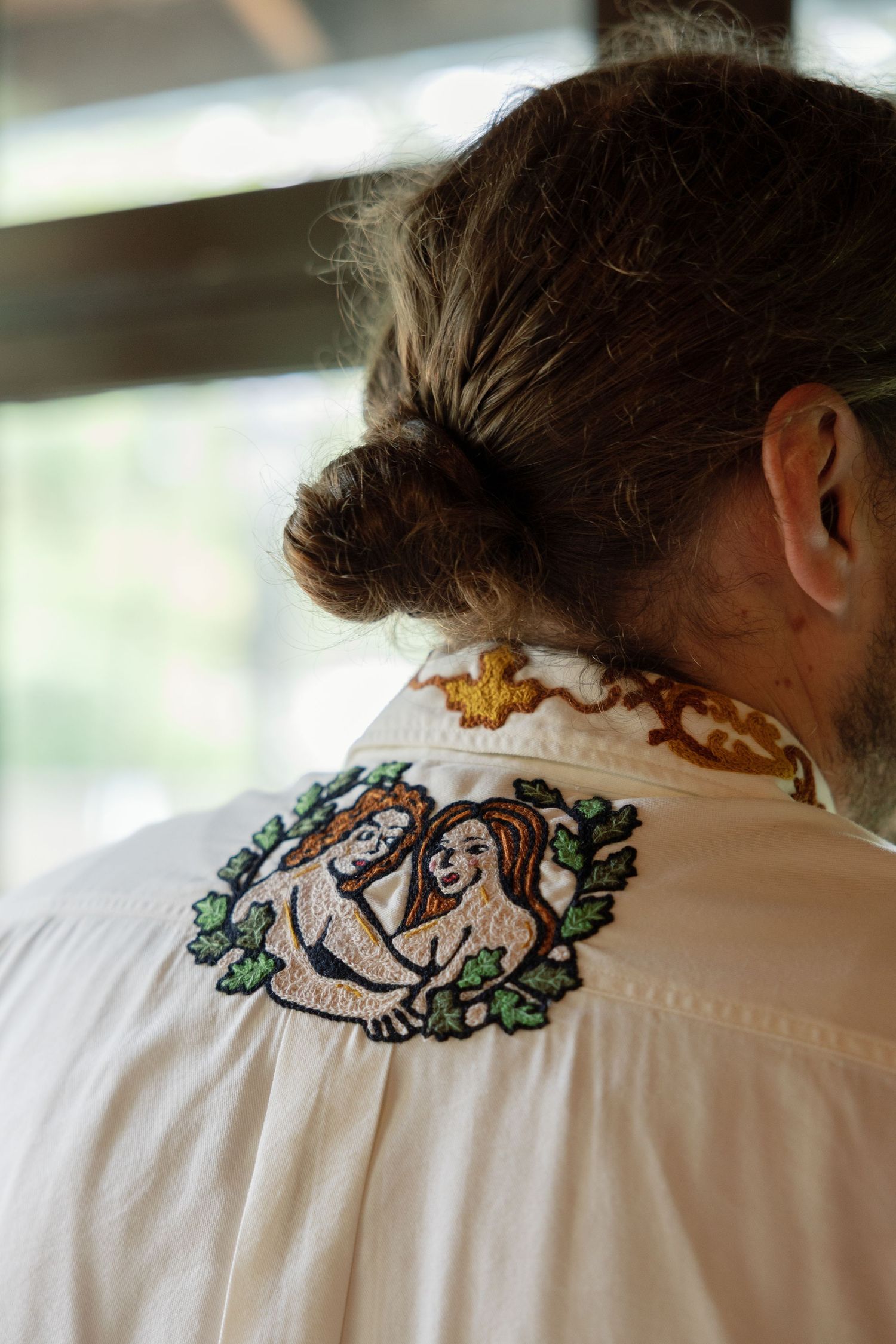 Back view of a white shirt with embroidered mermaid design and brown hair in a bun.