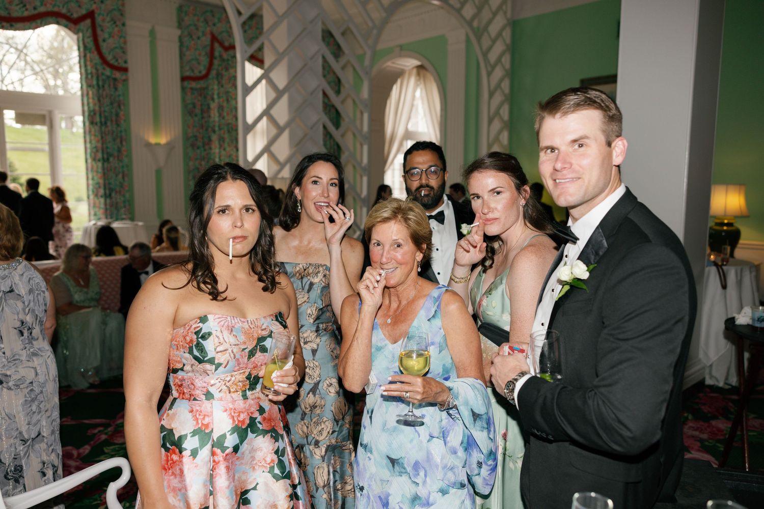 Group of elegantly dressed guests posing together at a formal wedding reception in a grand venue.