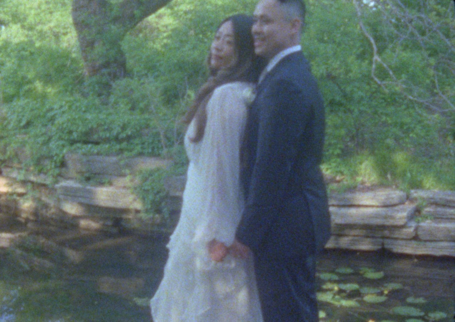 A couple shares a romantic moment together while standing by a creek in a lush outdoor setting.