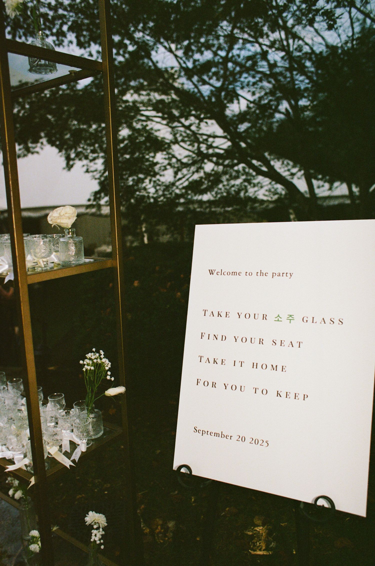 Decorative wedding signs with white text on stands displayed against a dark background with trees.
