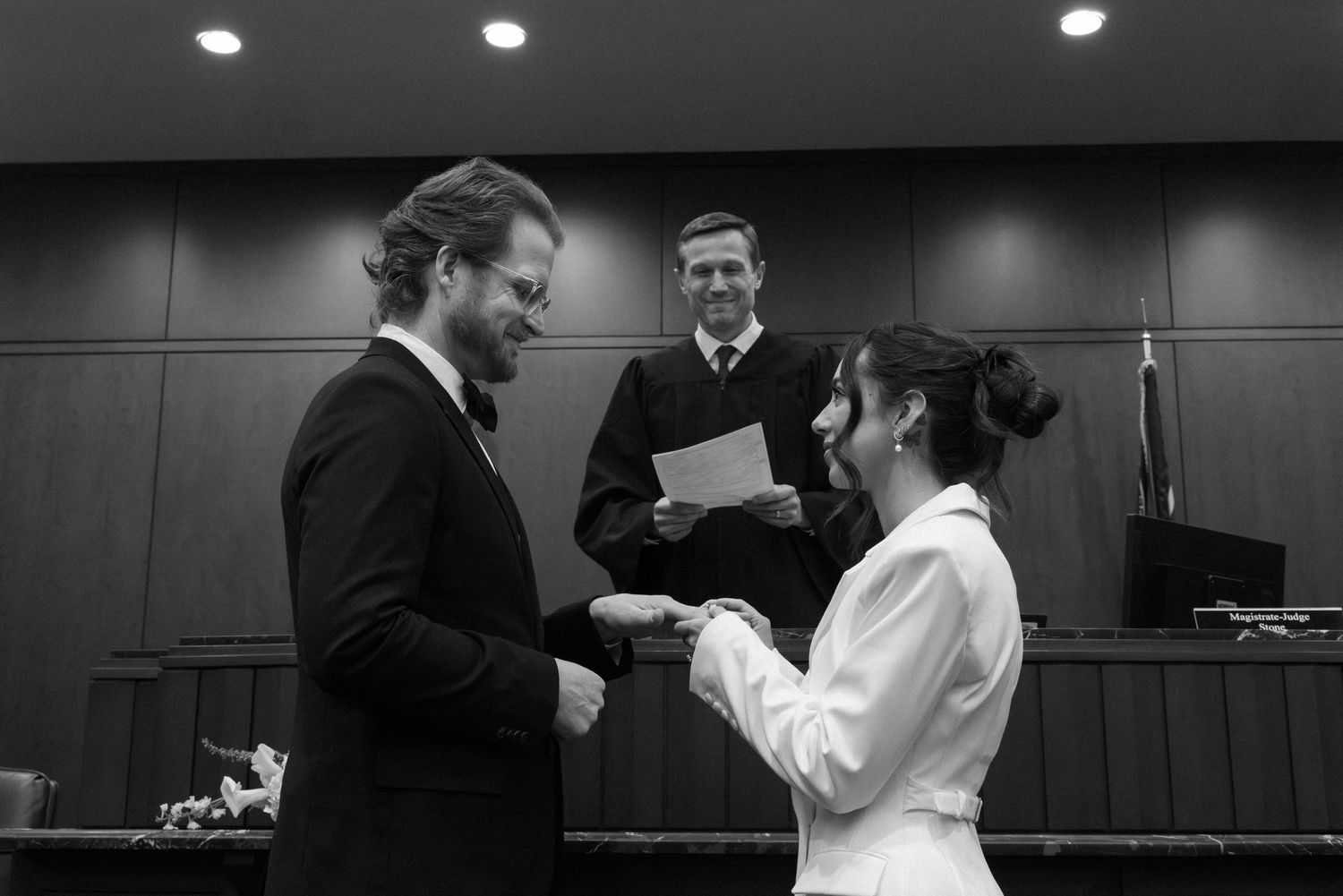 Black and white photo of a couple exchanging vows before a judge during a courthouse wedding ceremony.