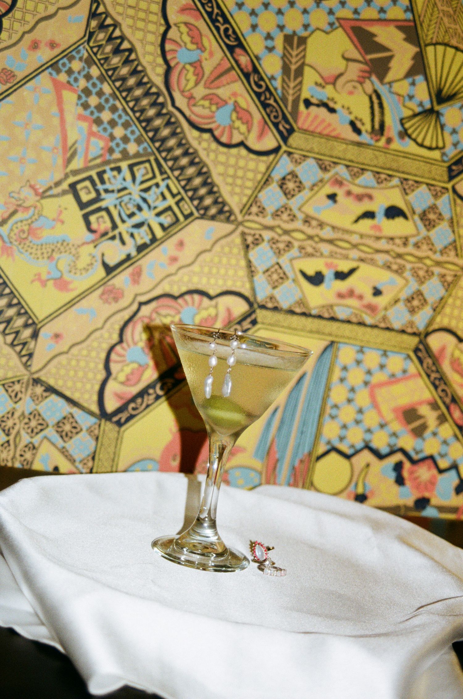 Martini glass rests on white napkin against ornate gold patterned wallpaper with geometric and floral designs.