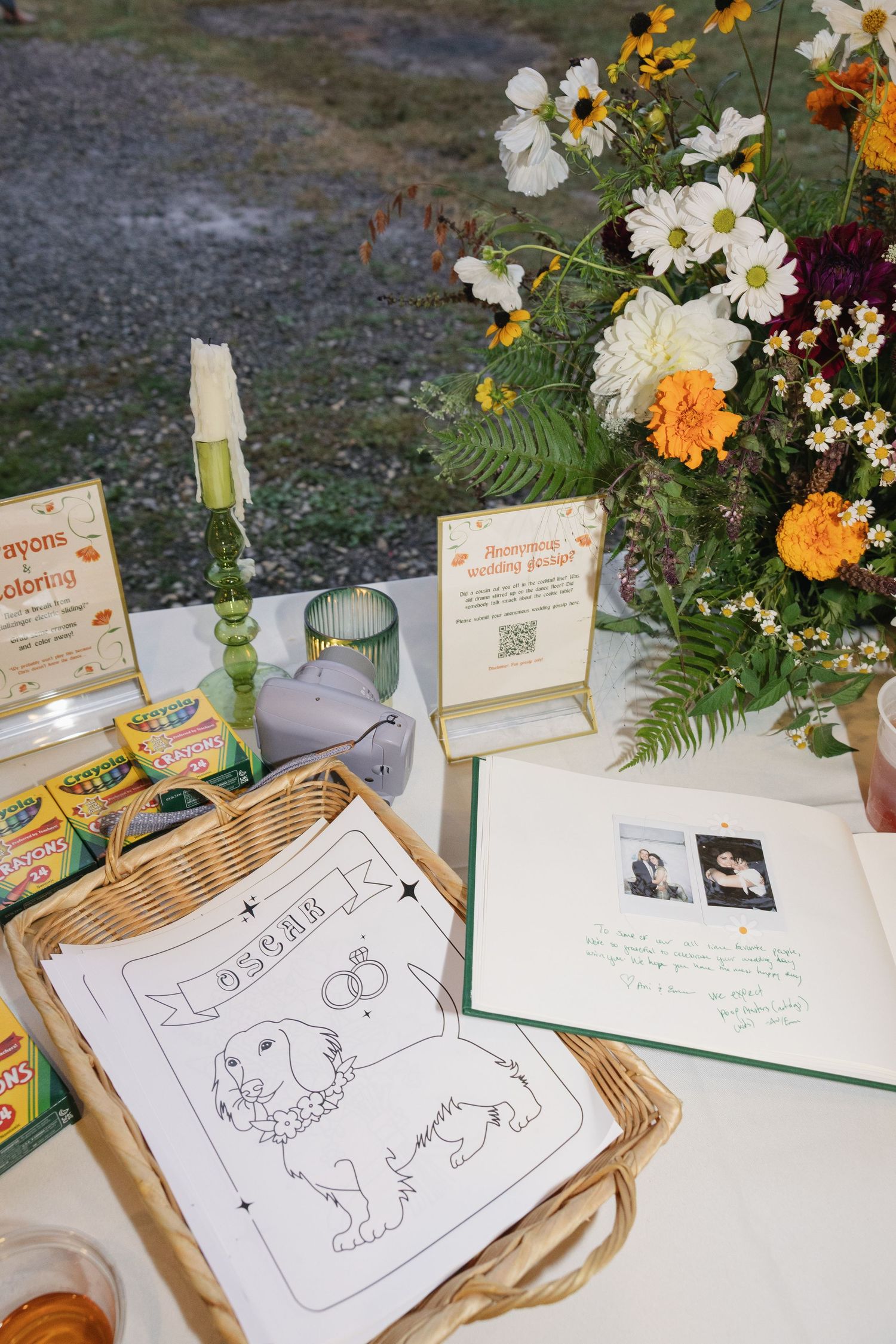 A guest book table at a wedding reception features coloring book pages, flowers, and decorative signs.