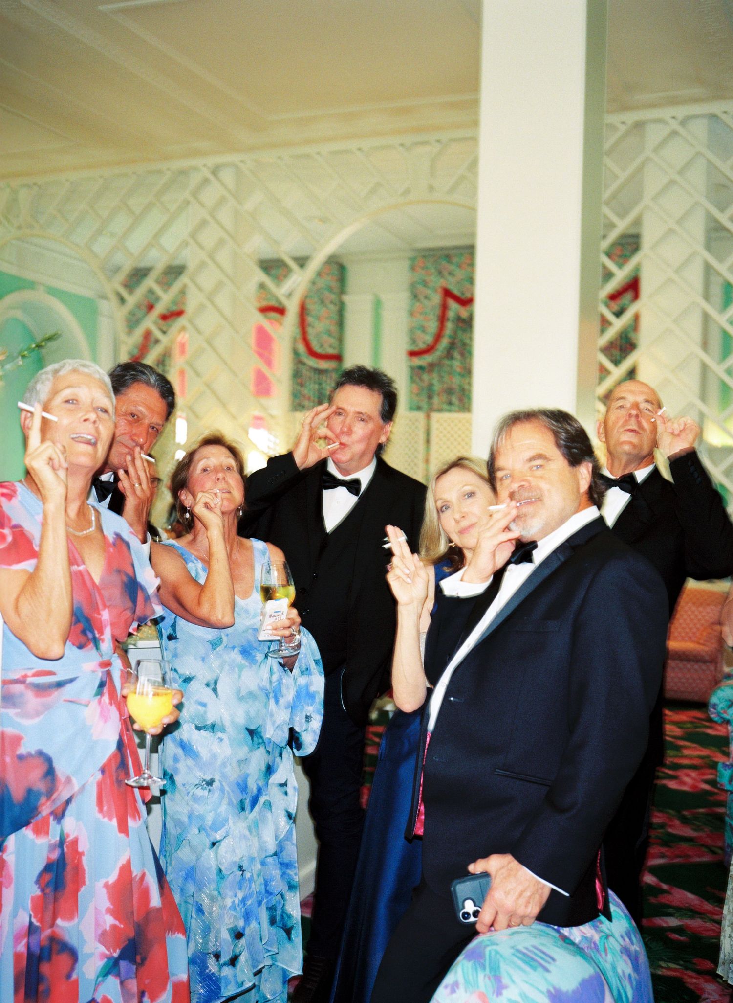 Elegantly dressed guests in formal attire laughing and celebrating at an upscale evening party or wedding reception.