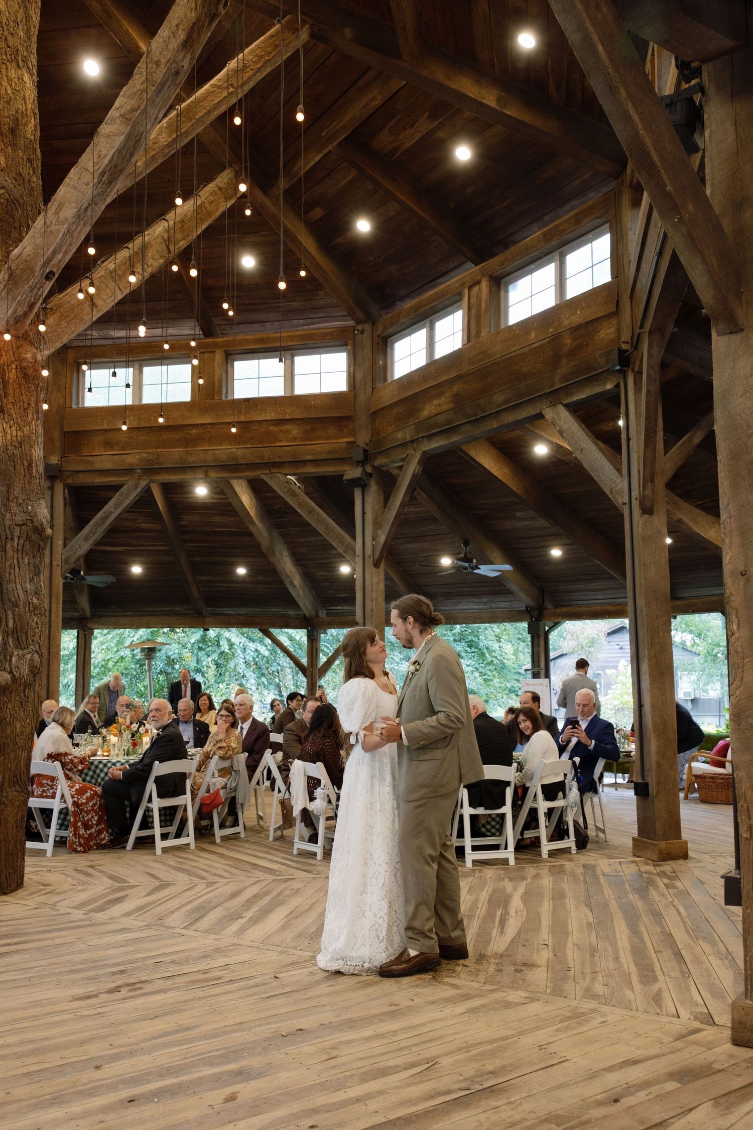Rustic barn wedding ceremony setup with wooden beams, string lights, and white folding chairs arranged in rows.