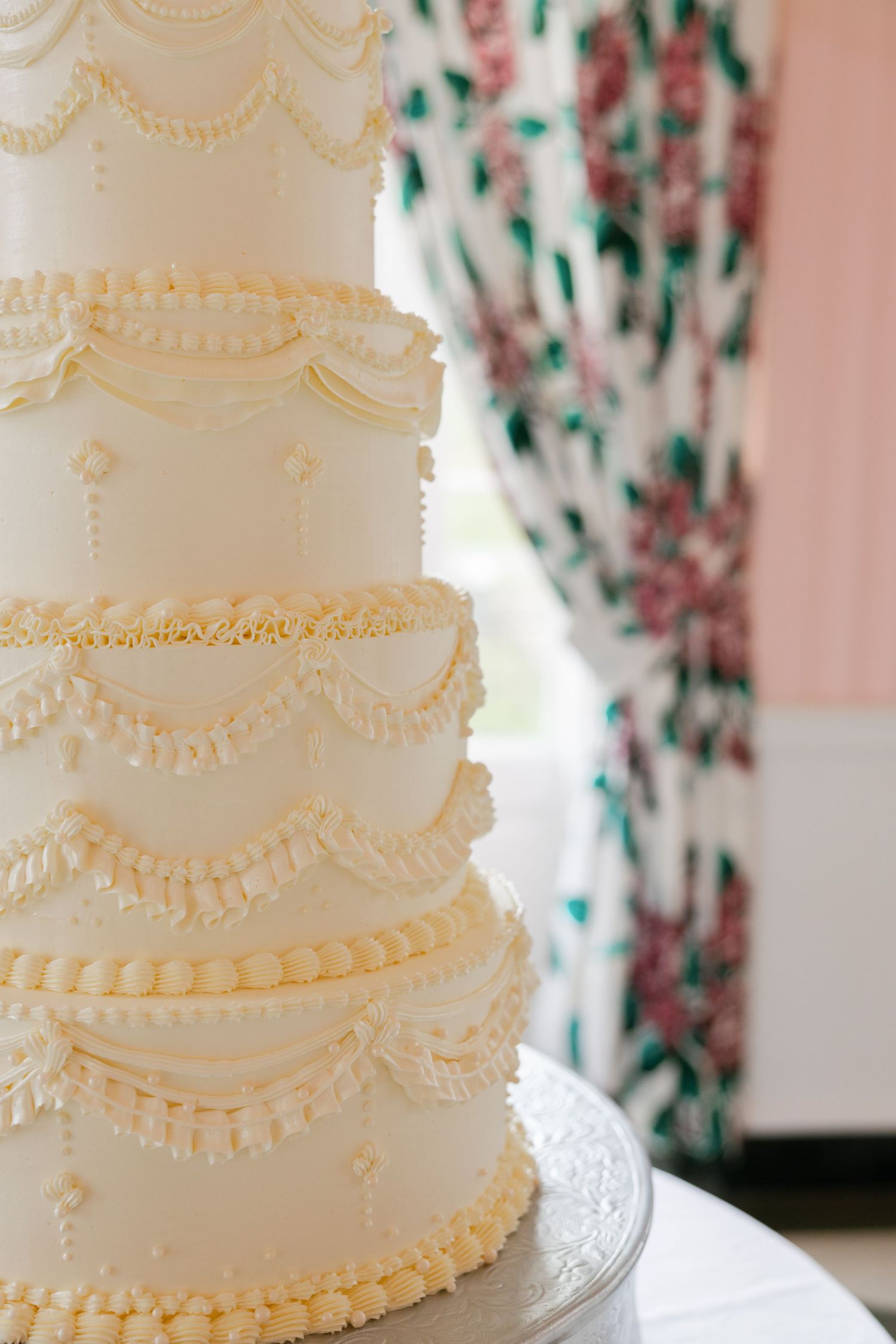 Elegant multi-tiered white wedding cake with intricate piped frosting details and swag decorations on a silver stand.
