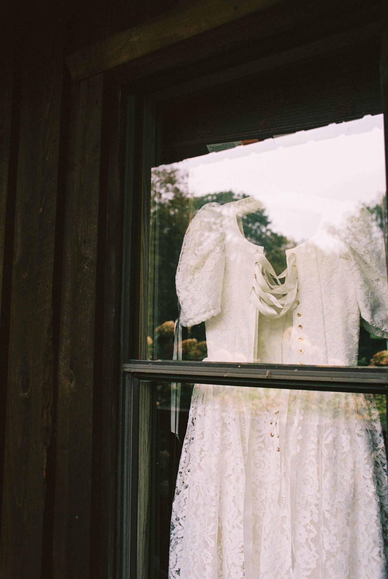 A row of white lace wedding dresses displayed on hangers against a dark background in a bridal boutique window.