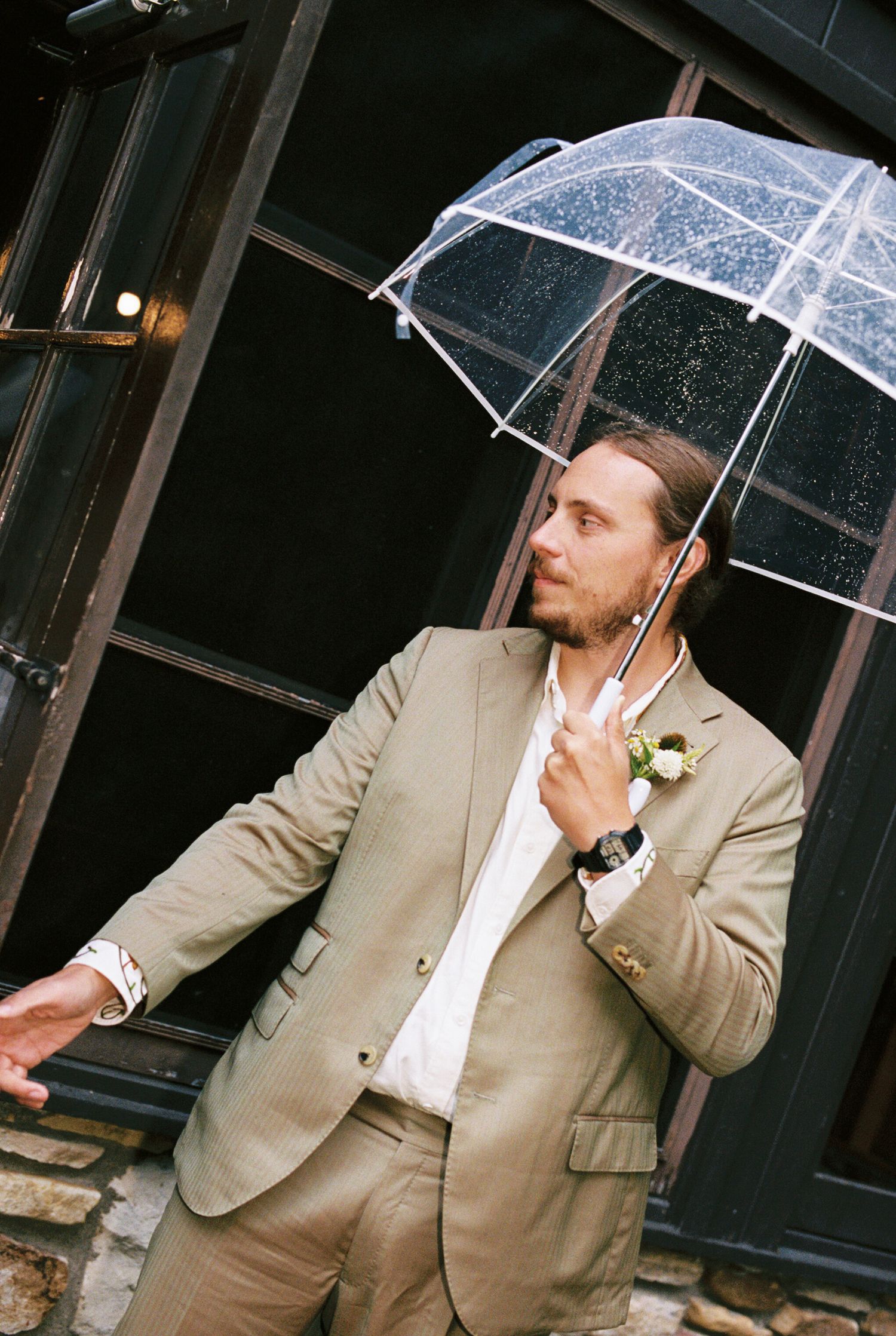 Man in beige suit and white shirt poses with clear umbrella in sequence of artistic portrait shots.