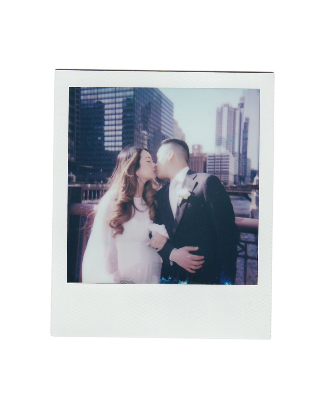 A romantic polaroid photo of a couple sharing a kiss on a rooftop with city skyscrapers in the background.