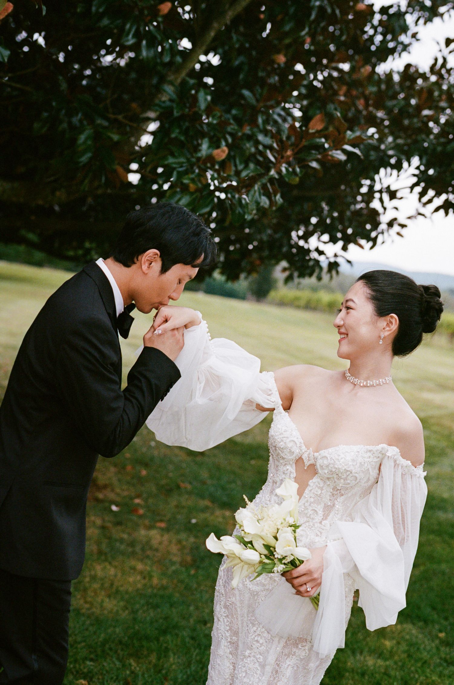A romantic wedding couple shares intimate moments under trees during an outdoor photo session.