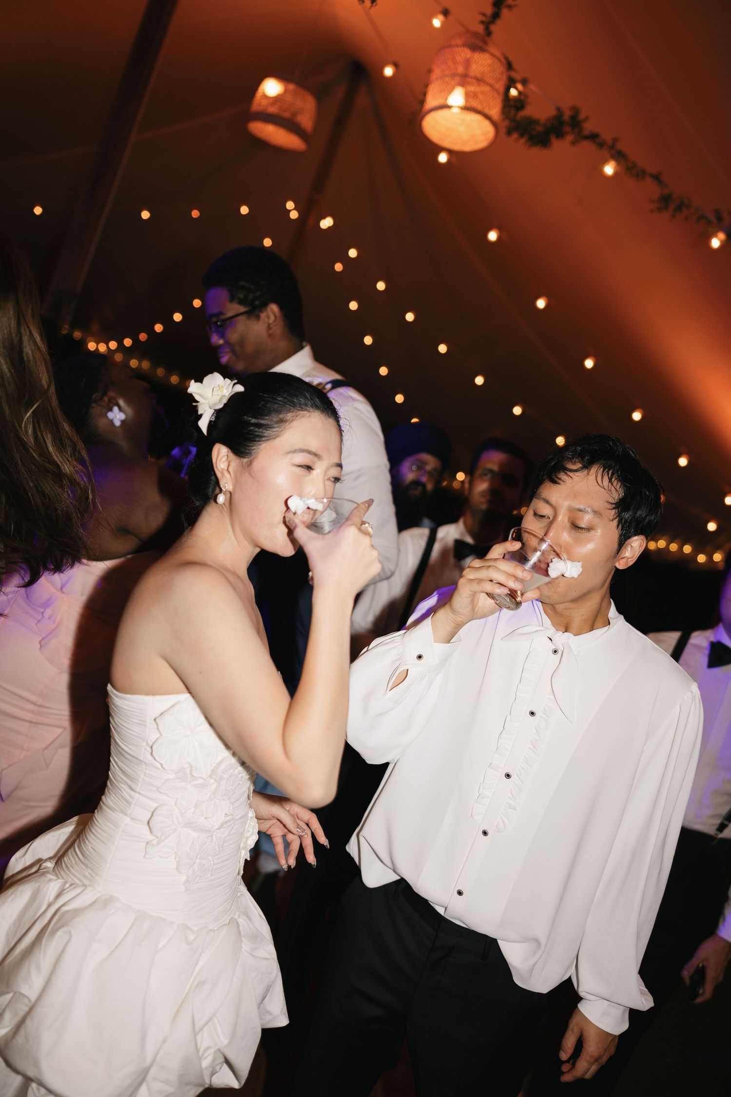 A sequence of candid dance floor moments at a wedding reception with guests in white attire under warm lighting.