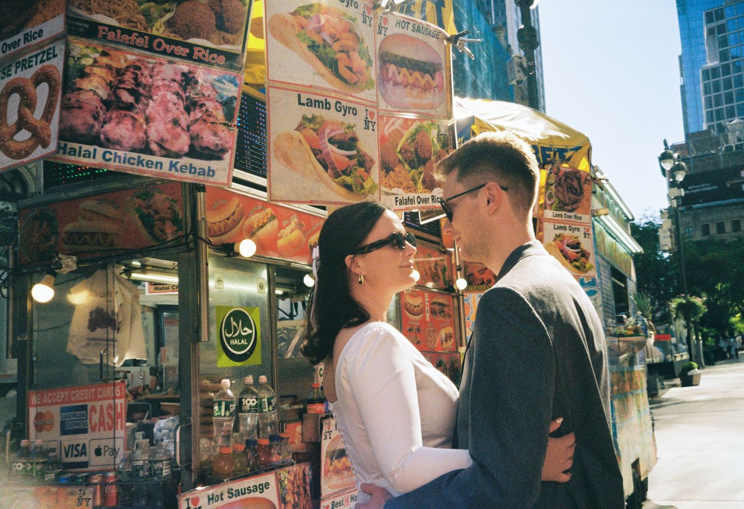 Couple sharing a romantic moment in front of a NYC street food cart with colorful menu signs.