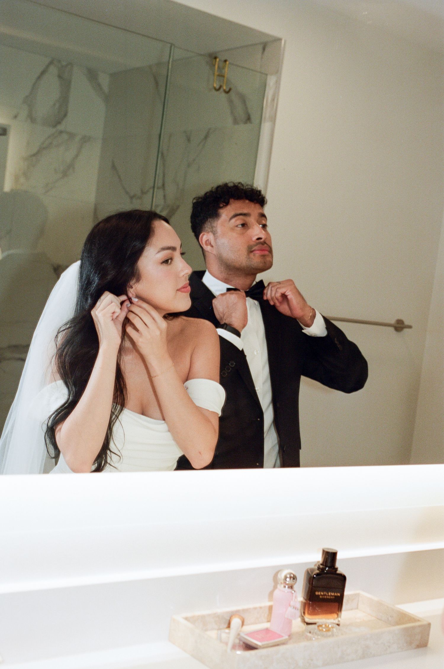 A couple in formal wedding attire brushes their teeth together at a bathroom sink.