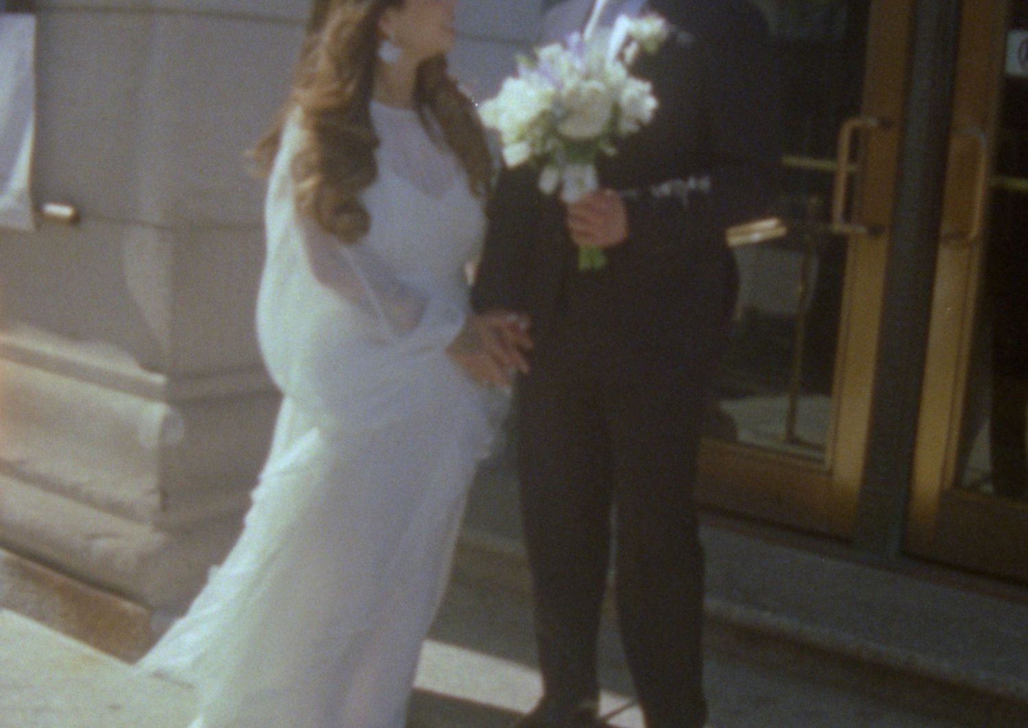 A couple stands together at a wedding ceremony, with the bride wearing a flowing white dress and holding a bouquet.